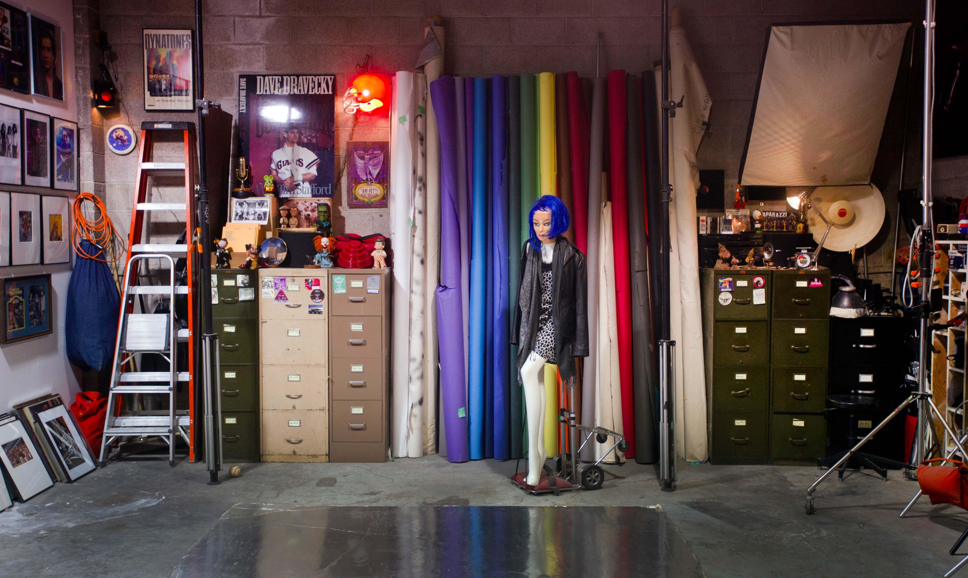 A studio space featuring a mannequin with blue hair positioned among colorful backdrops and various studio equipment.
