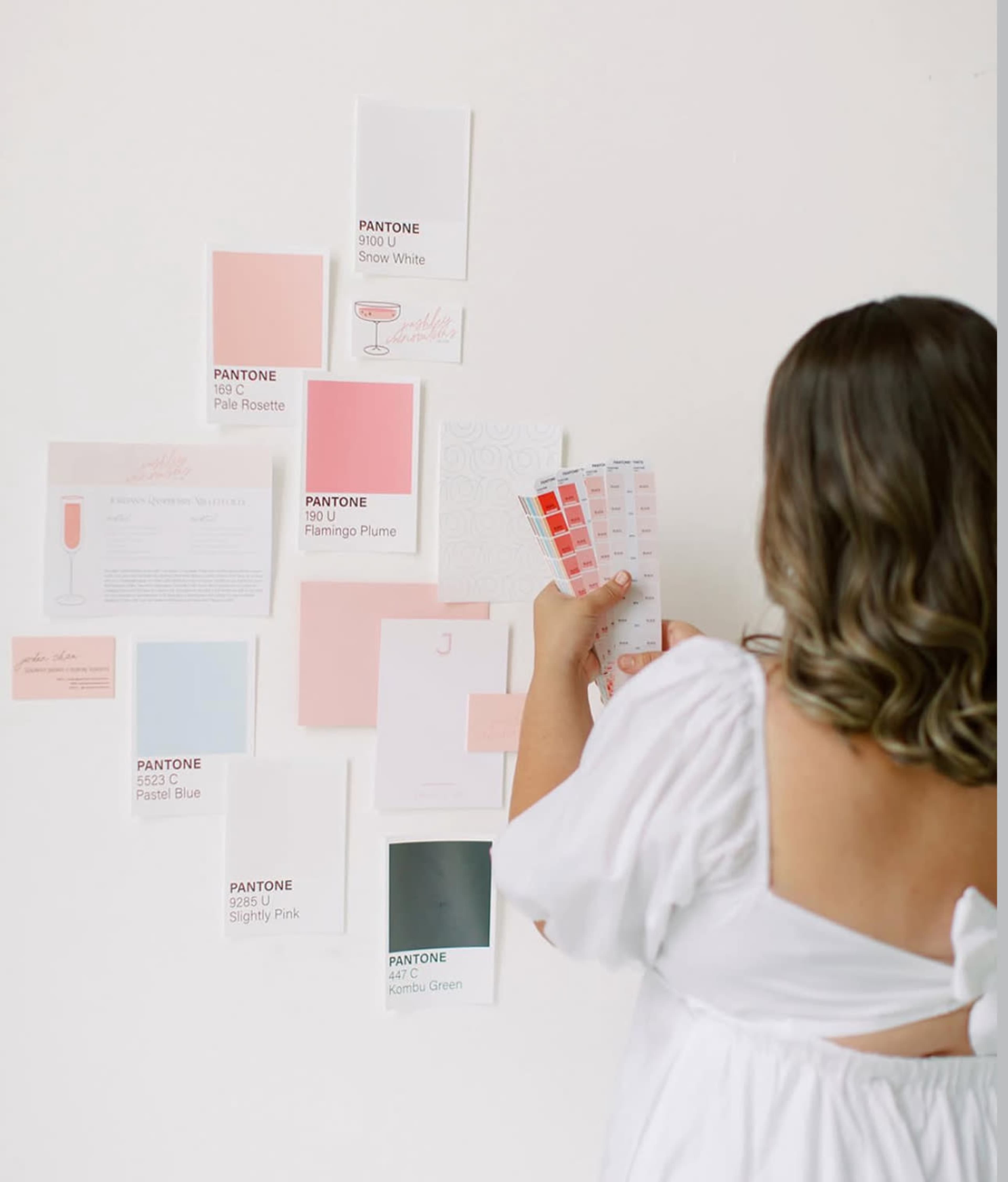 A person is arranging various color swatches and design materials on a white wall.