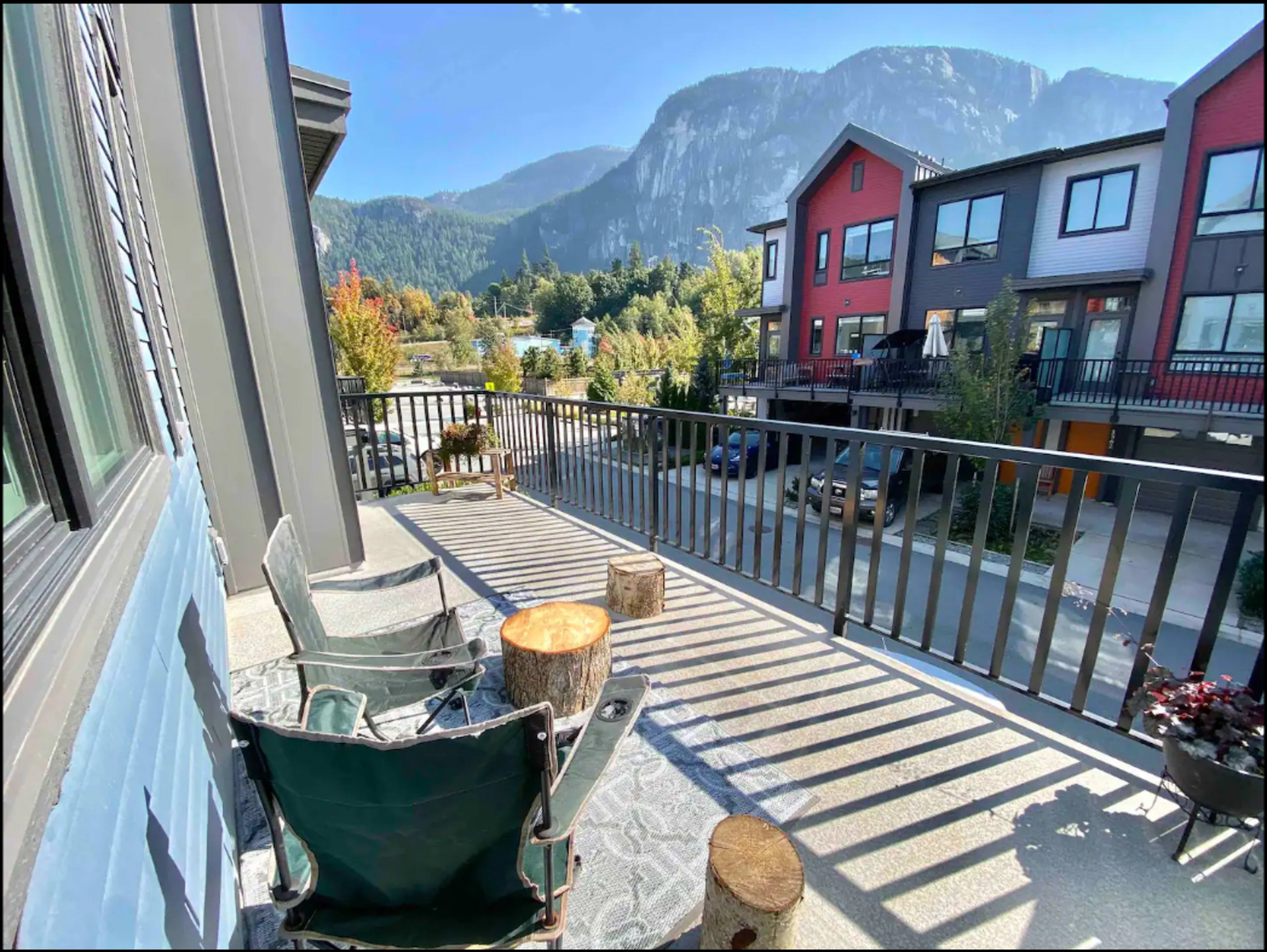 A balcony with two green chairs and wooden stumps overlooks a neighborhood and mountains in the background.
