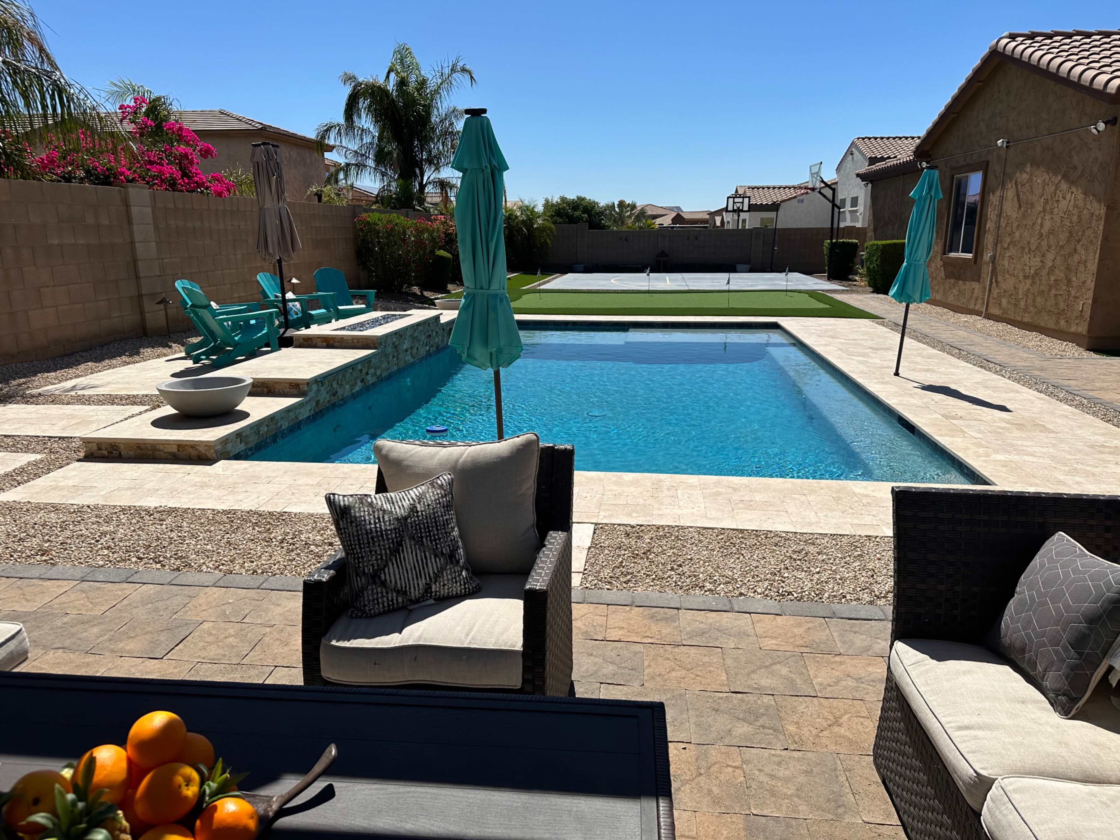 The image shows a backyard with a swimming pool, lounge chairs, and a putting green, surrounded by a stone patio and landscaped walls.