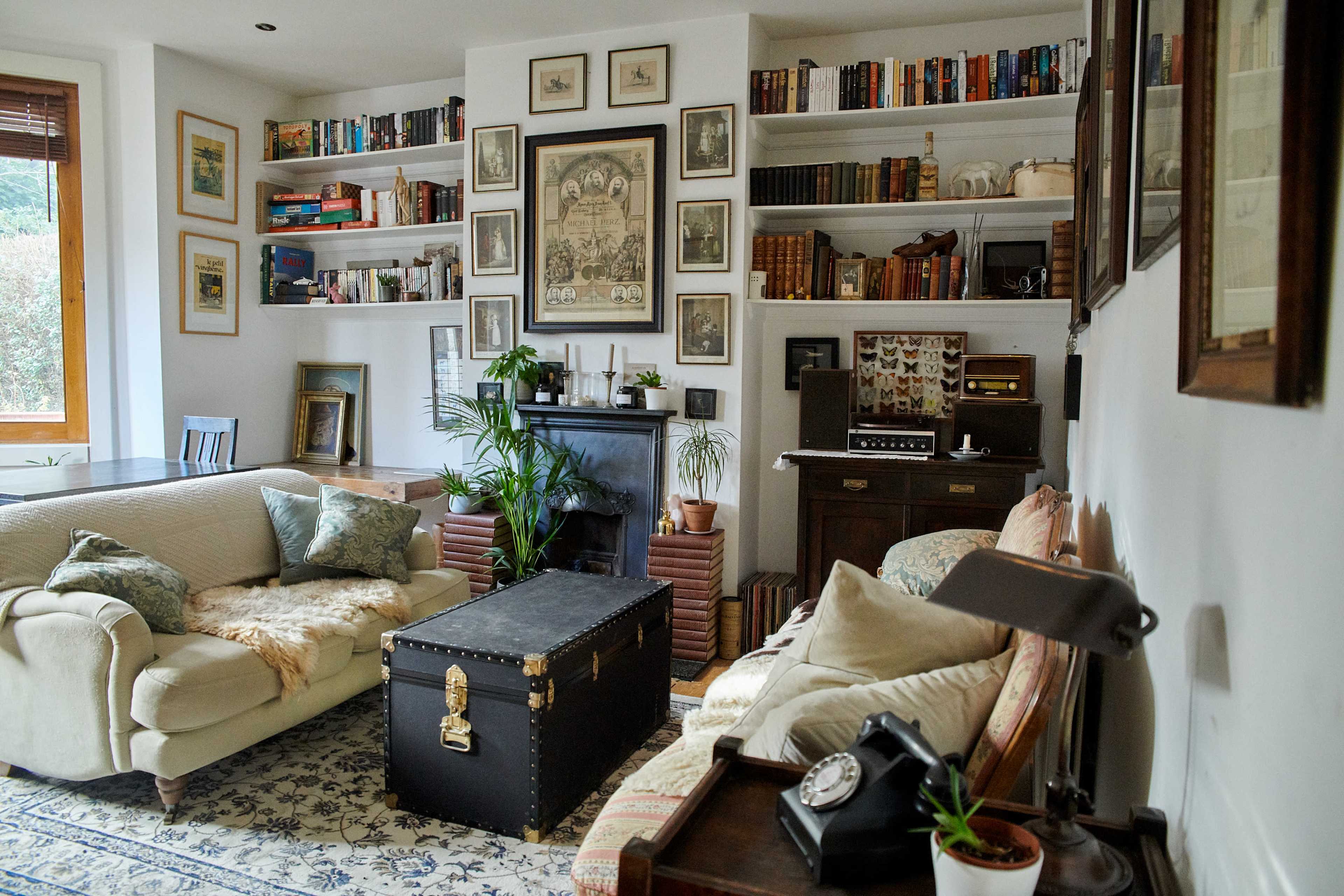 A cozy living room with bookshelves lined with books, a vintage record player, and two sofas arranged around a coffee table.