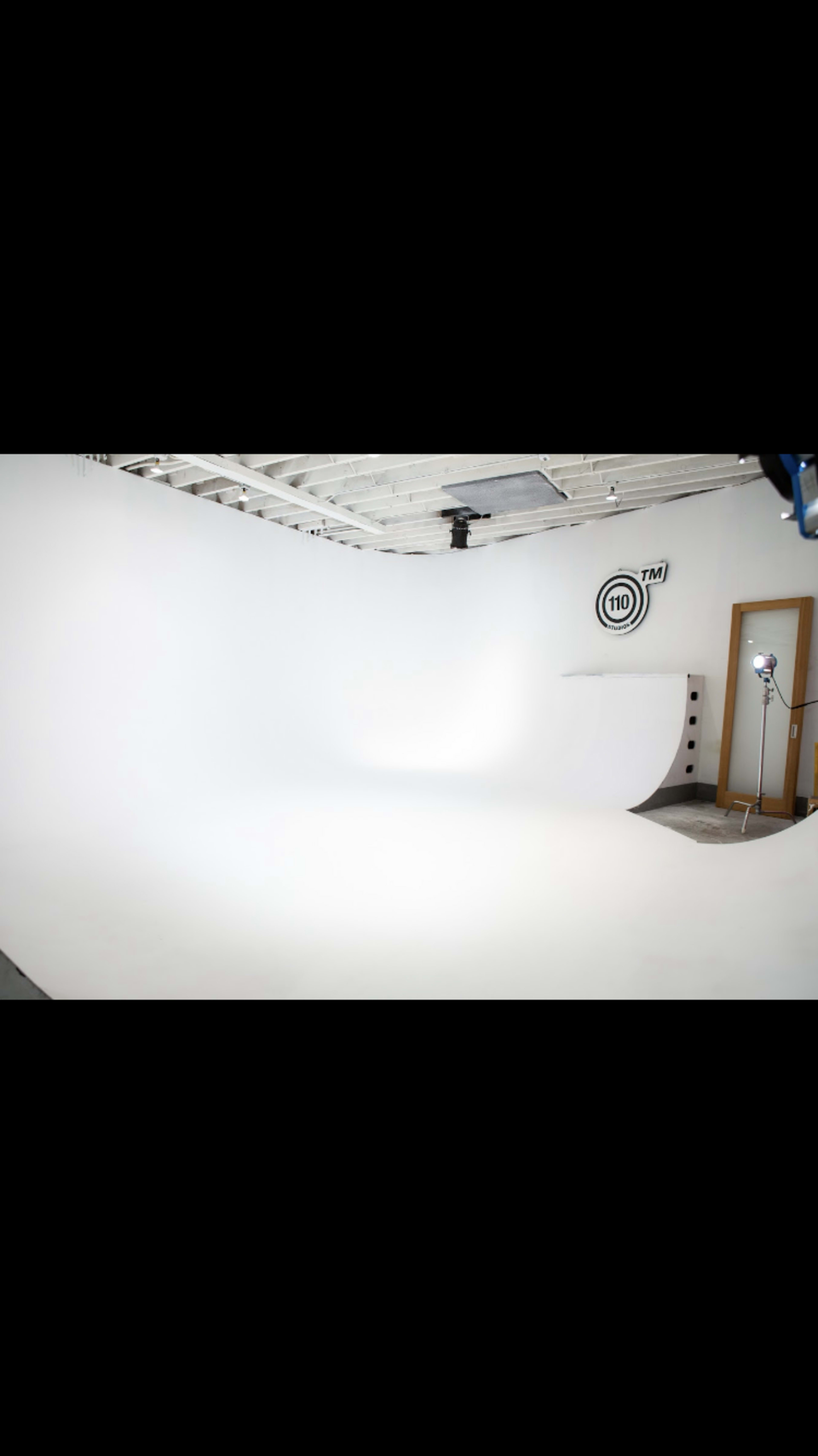 The image shows a spacious photography studio with a seamless white backdrop and a light setup in the corner.