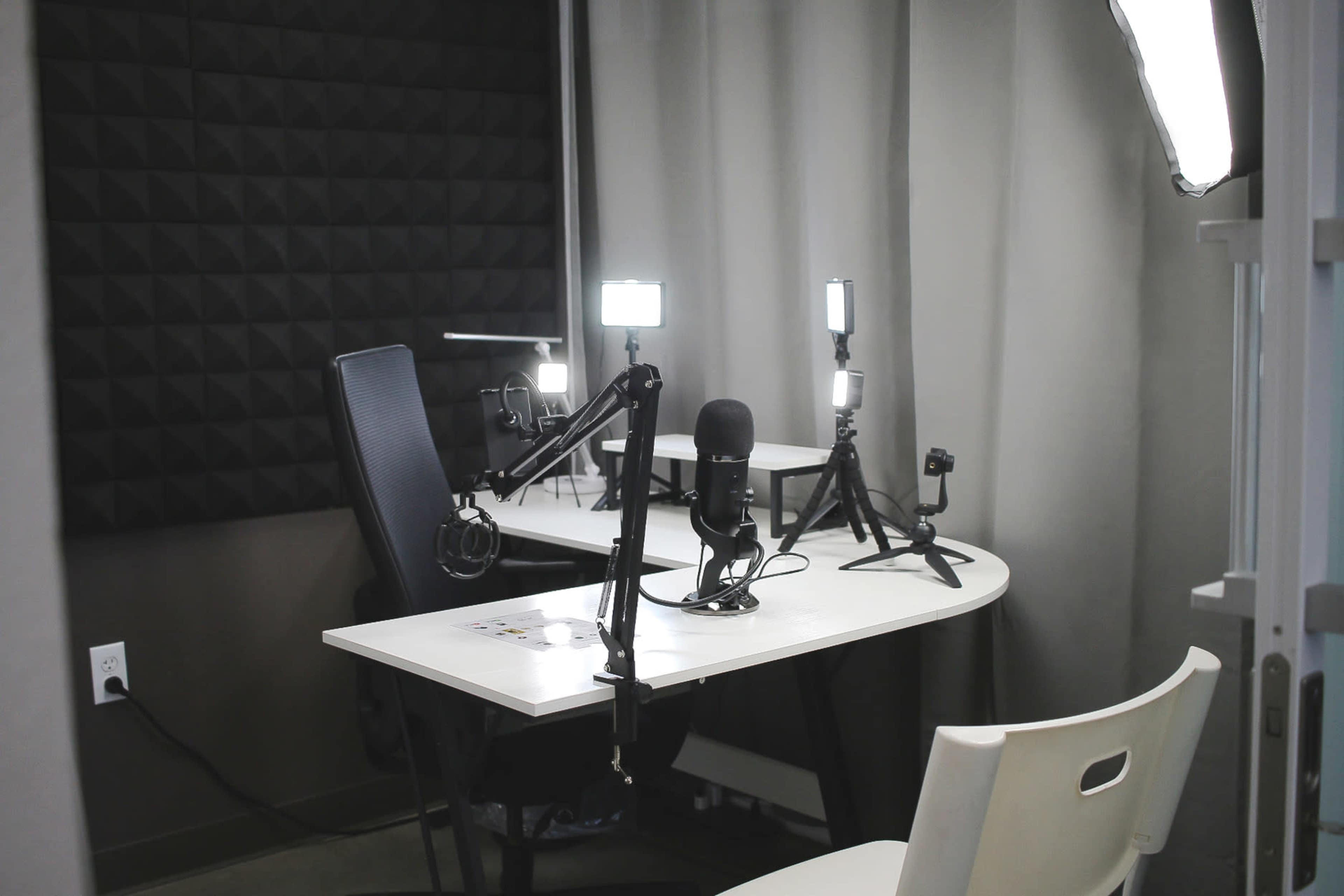 A small recording studio setup with microphones, cameras, and lighting equipment on two desks.