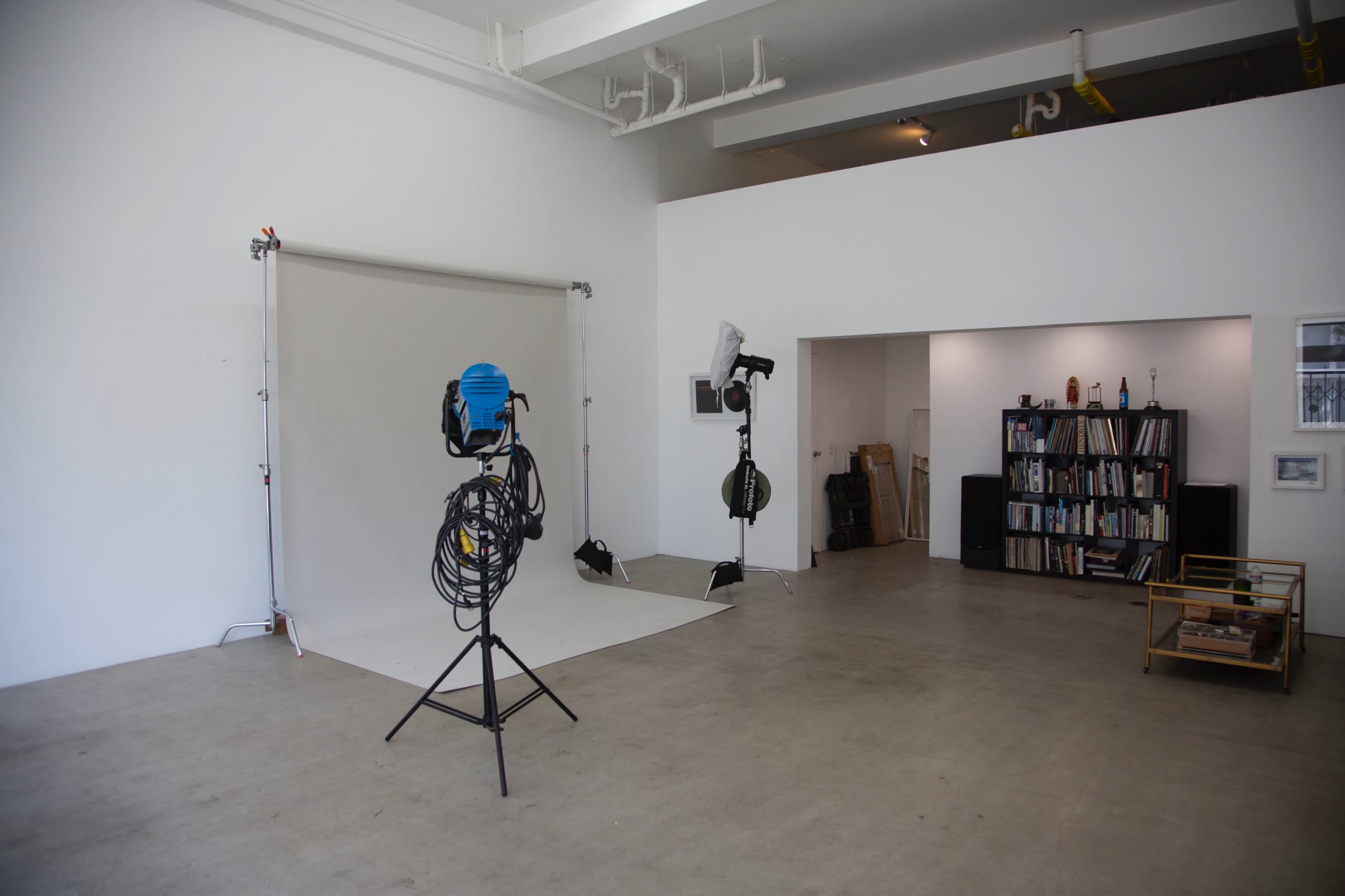 A spacious studio with a white backdrop, studio lighting equipment, and a shelf filled with books.