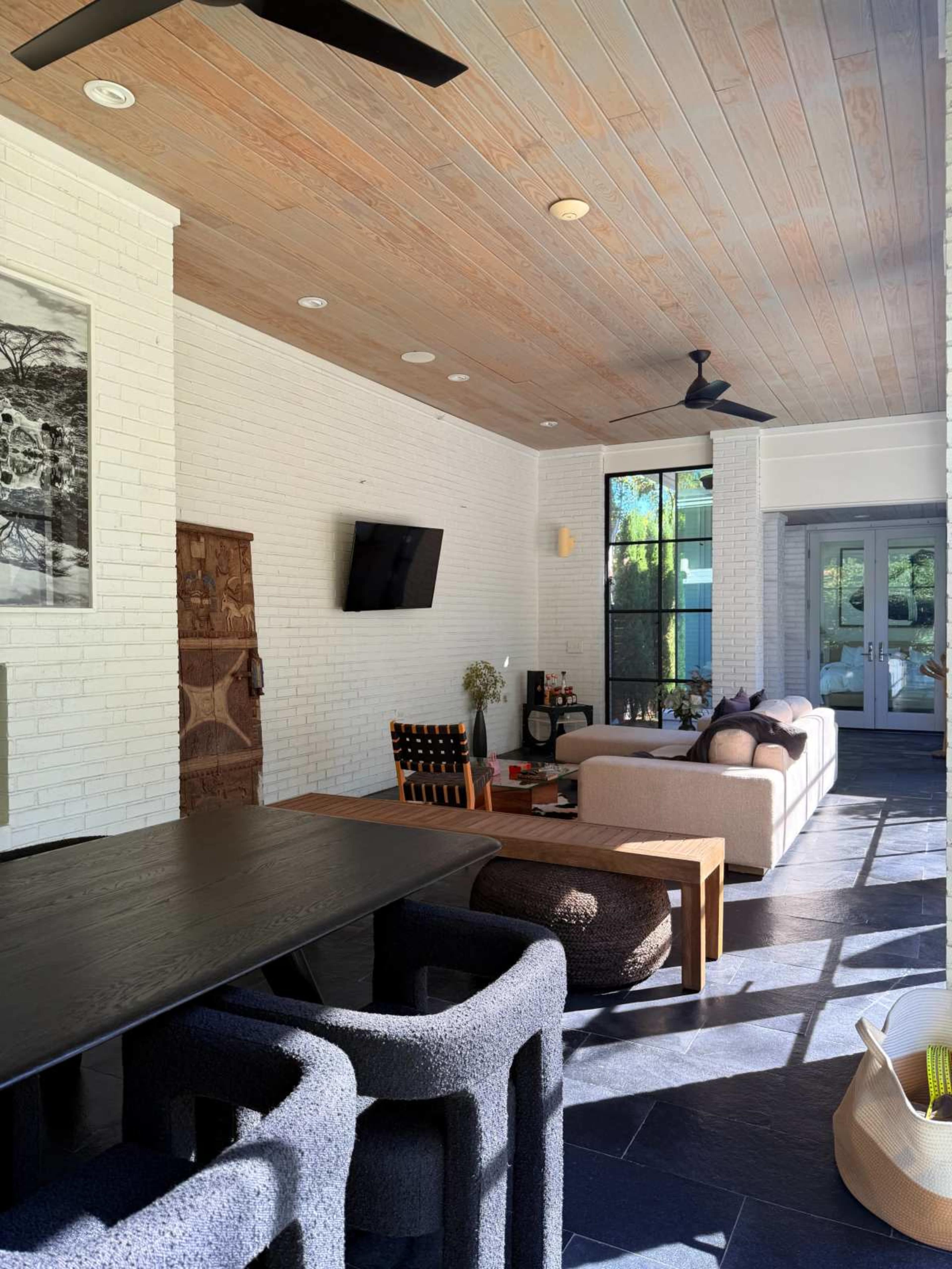 The image shows a modern living space with a white brick wall, a wooden ceiling, and a seating area that includes a sofa and a dining table.