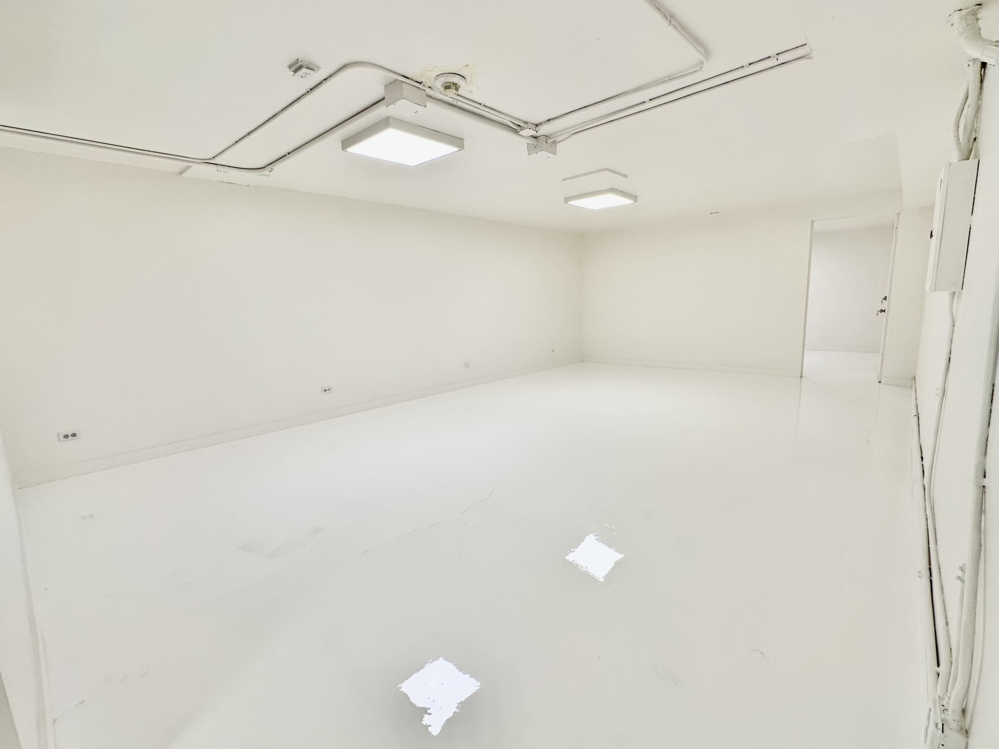 An empty, well-lit room with white walls and a glossy white floor.