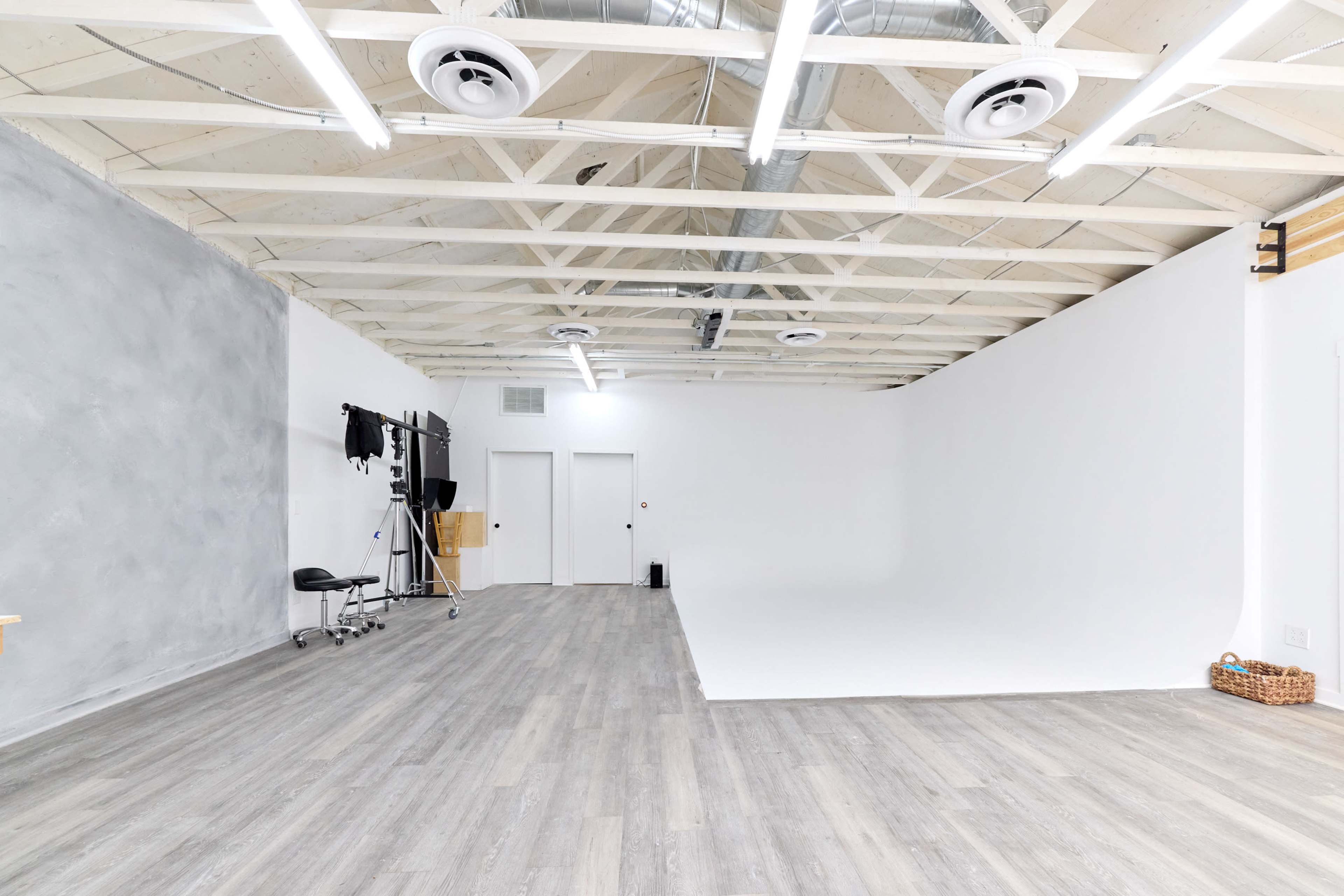 A spacious photography studio featuring a white backdrop, wooden flooring, and a few pieces of equipment against one wall.