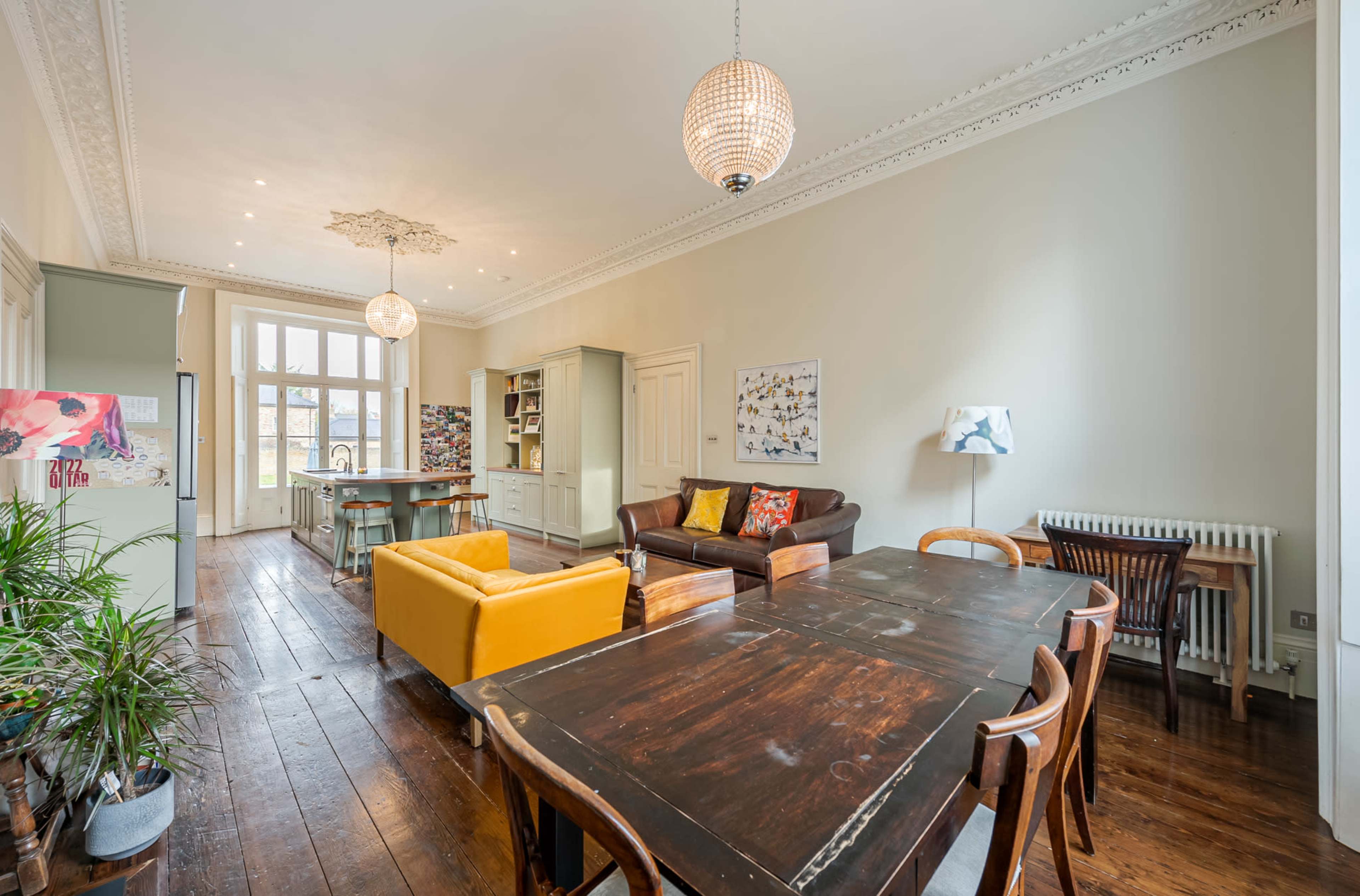 A spacious living area with a dining table, a yellow couch, and large windows allowing natural light to enter.