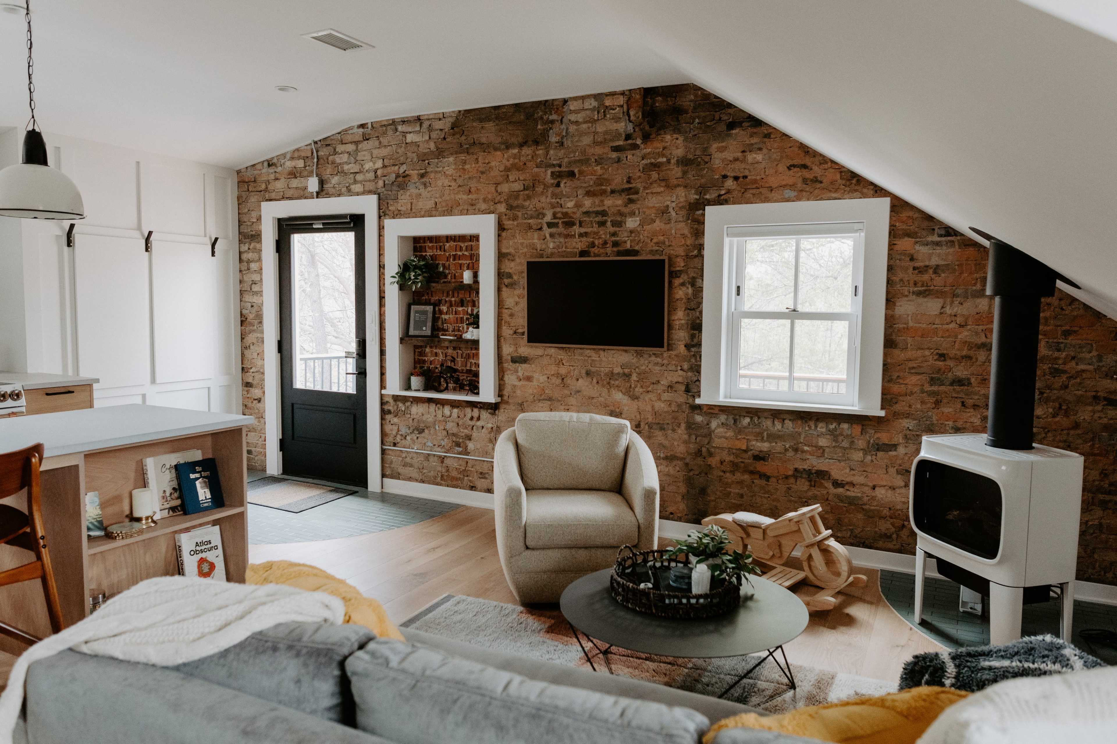 A cozy living room features a brick wall, modern furnishings, and a large window with natural light.