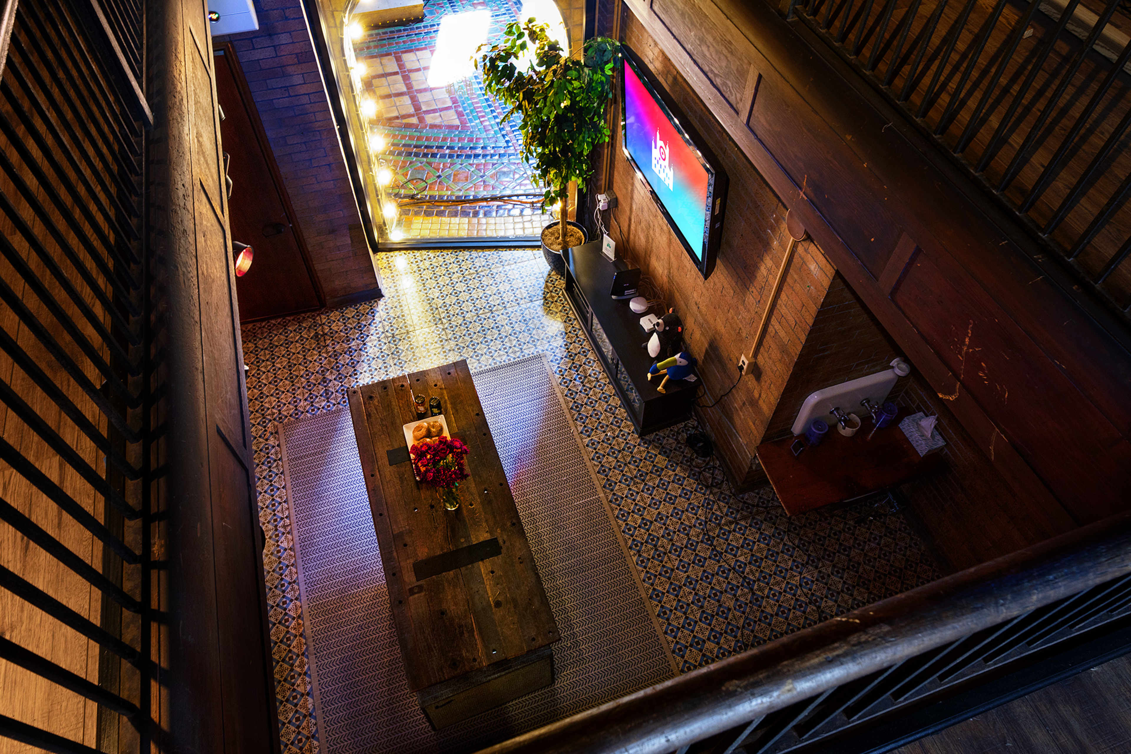An indoor space with a wooden coffee table, a plant, a large television mounted on the wall, and patterned tiles on the floor.