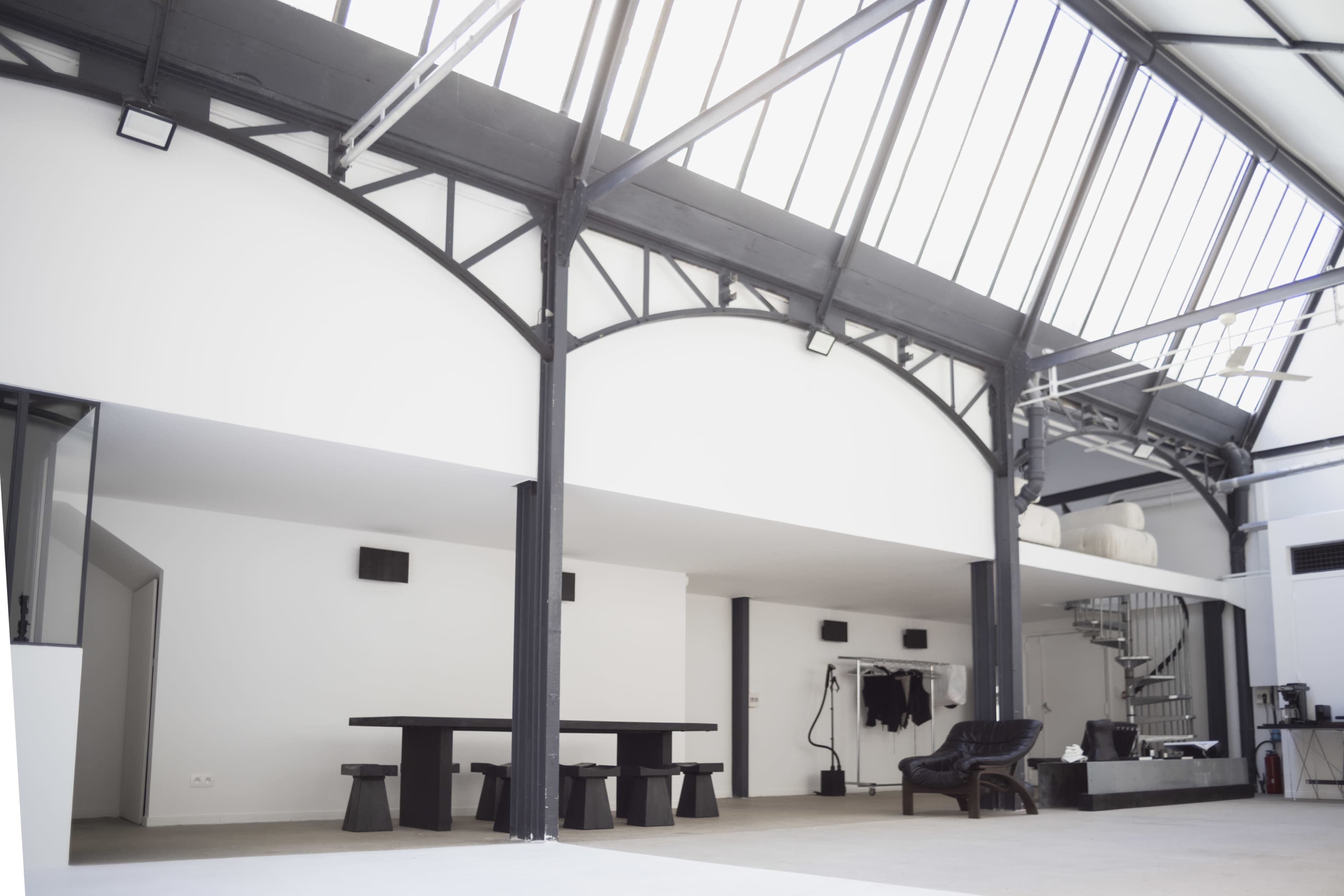 The image shows a spacious, modern interior of a building featuring high ceilings, a large table, and a spiral staircase.