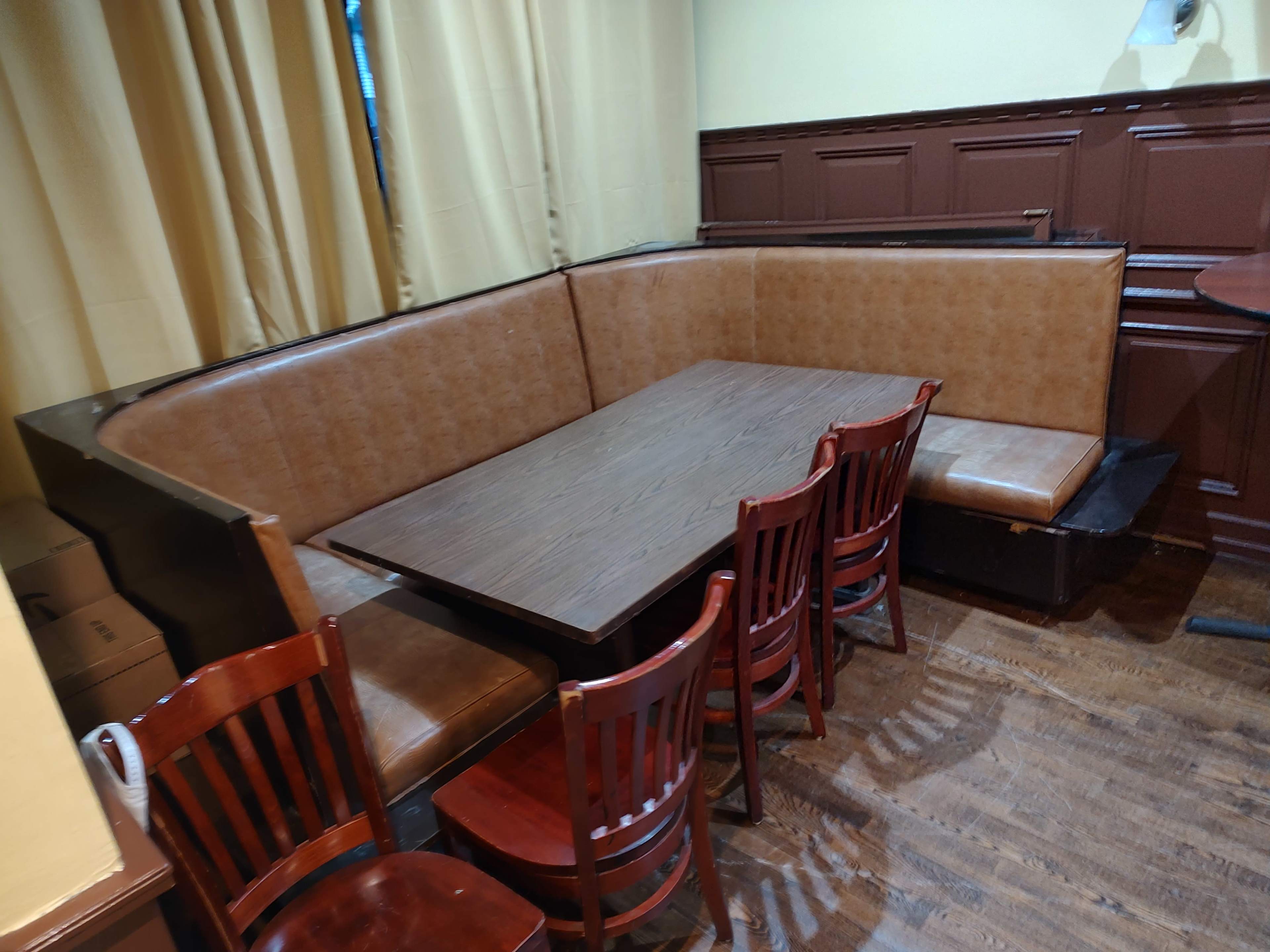 The image shows a dining area with a wooden table surrounded by brown chairs and a cushioned booth seating against the wall.