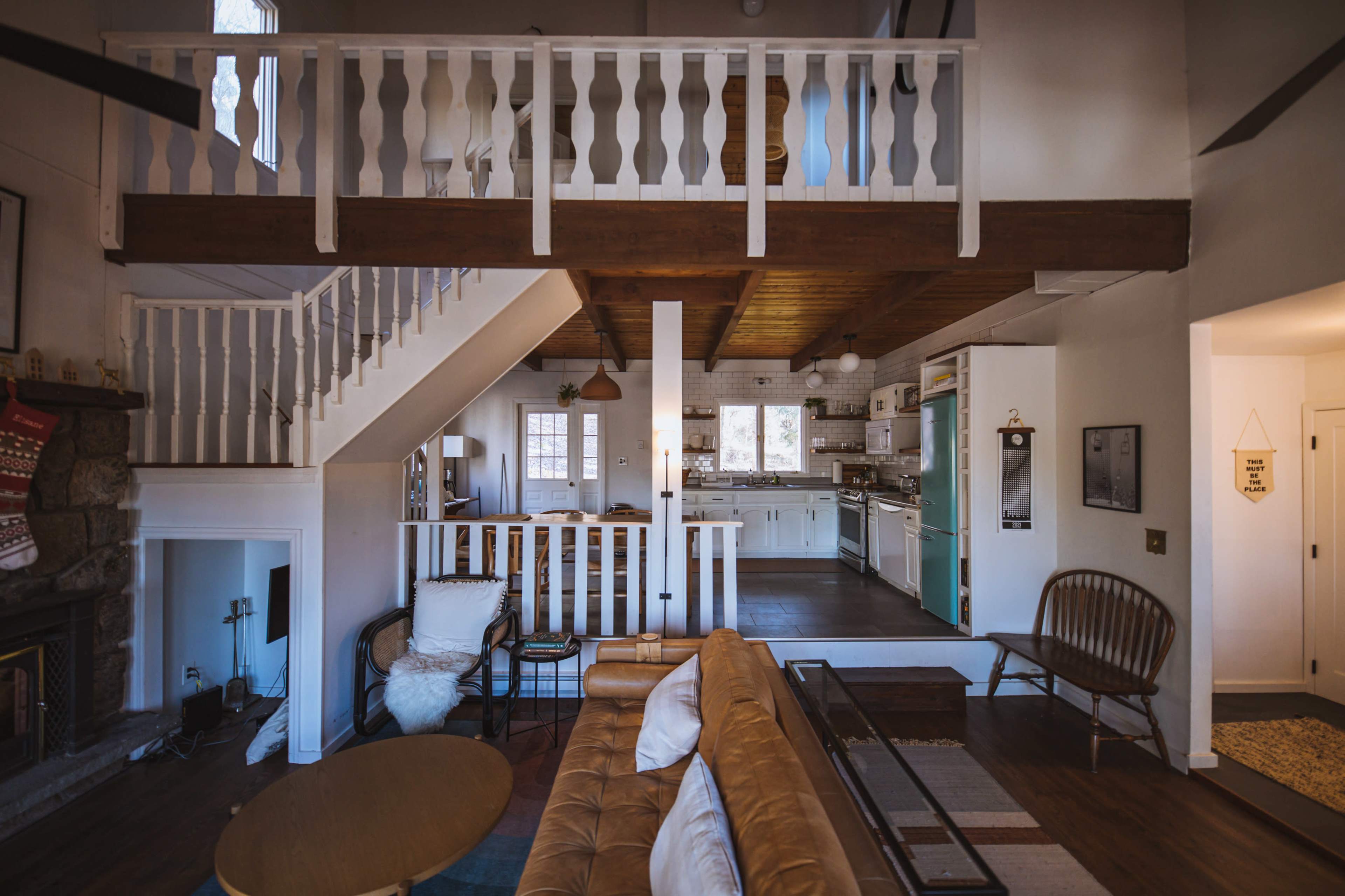A cozy, two-level living space with a wooden staircase, a balcony railing, and a sectional sofa facing a coffee table.