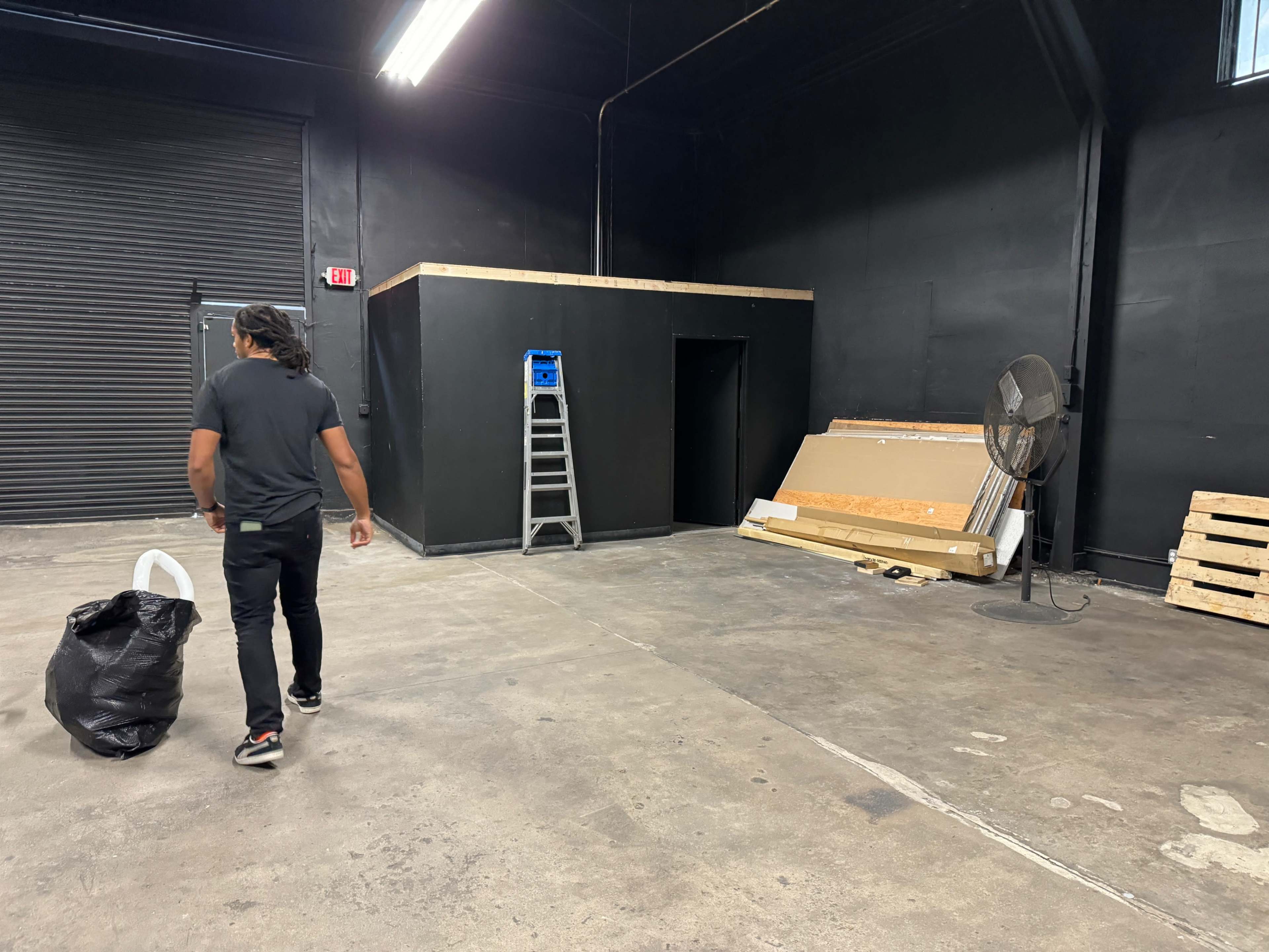 A person is walking away from a partially built structure in a dimly lit, empty warehouse space.