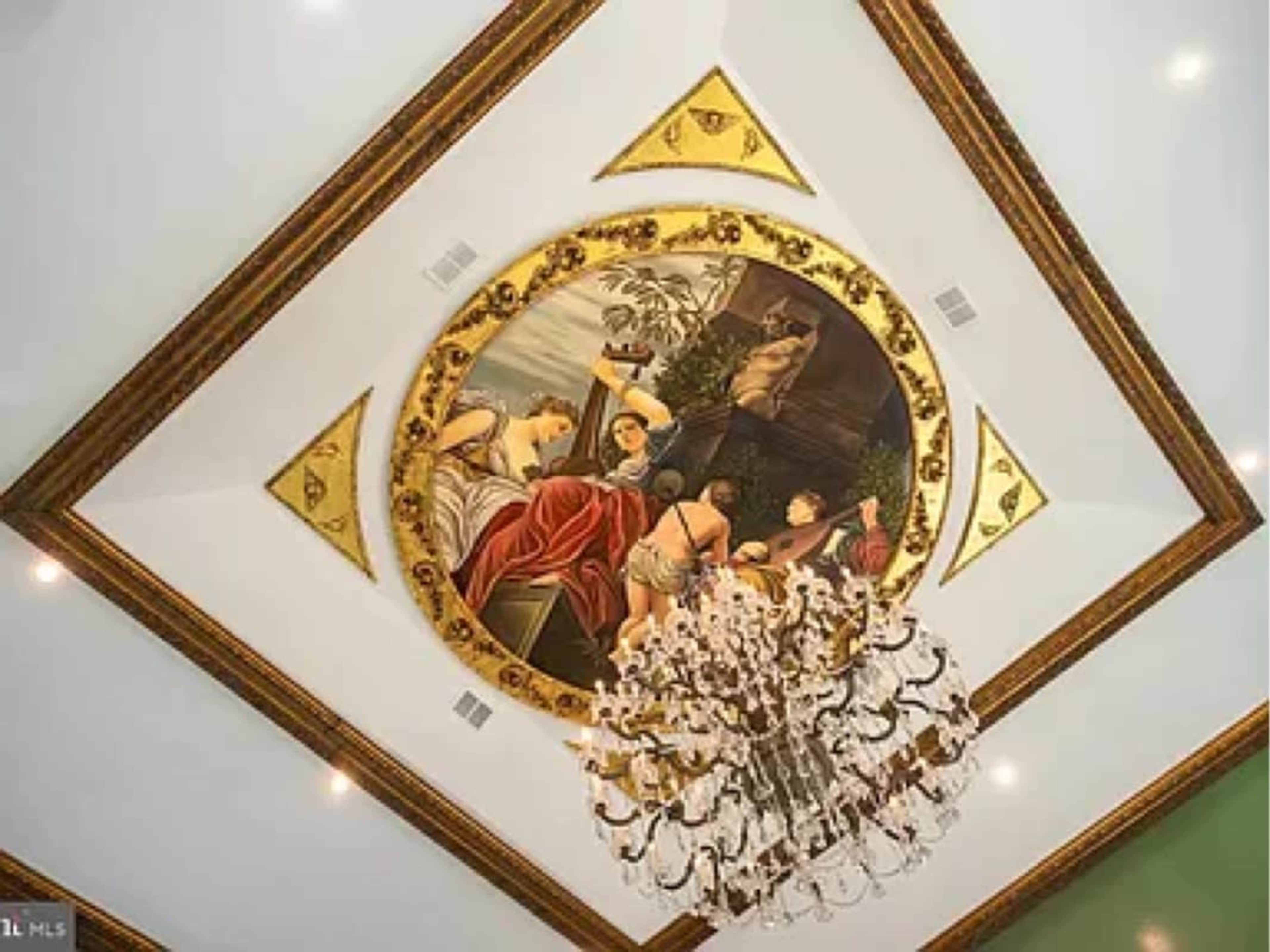 An ornate ceiling with a circular painting surrounded by gold accents and a large chandelier hanging below.