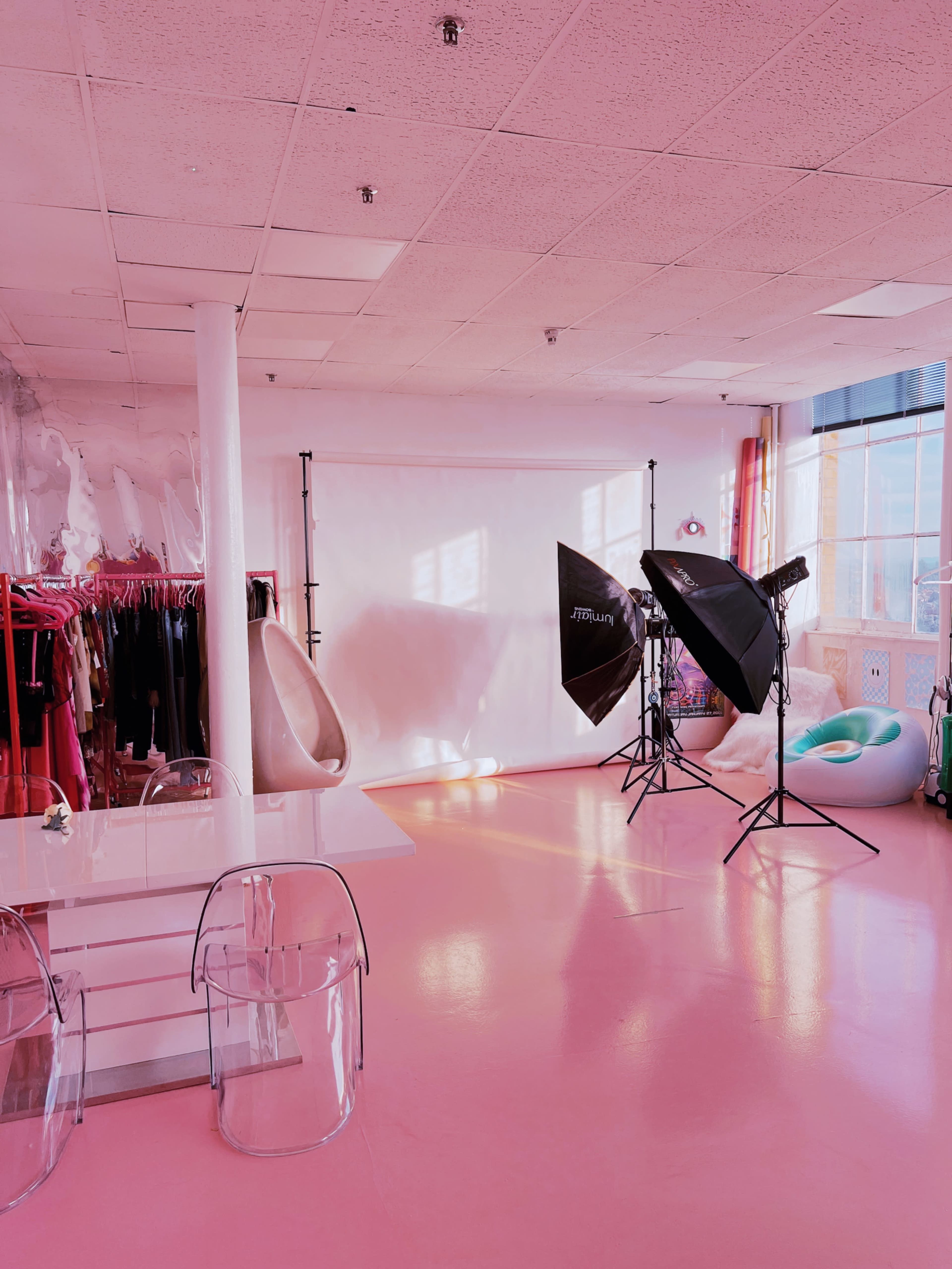 A brightly lit photography studio with a pink floor, a white backdrop, and various lighting equipment.