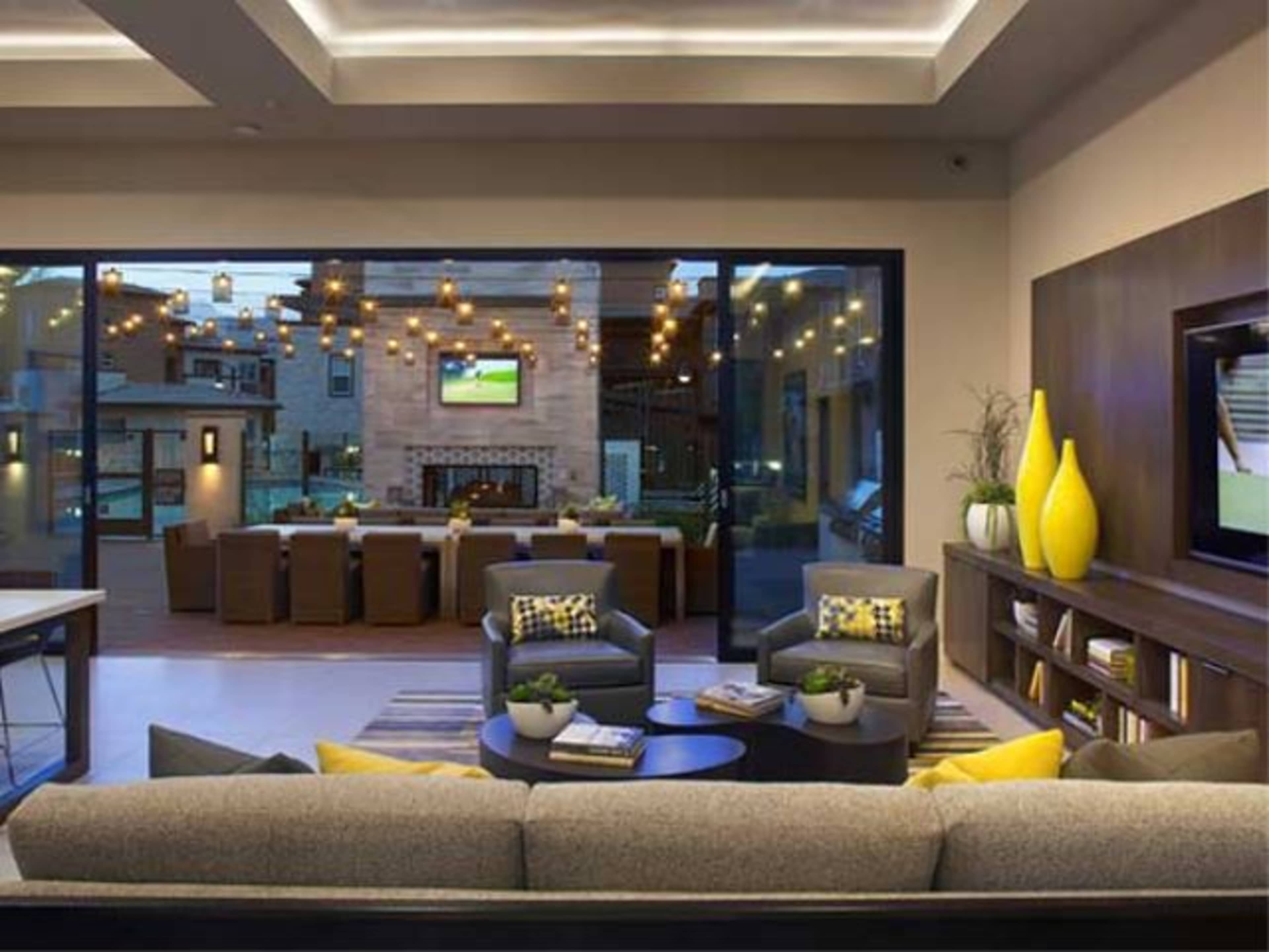 A modern living room features a large sectional sofa, a coffee table, and a view of an outdoor dining area illuminated by string lights.