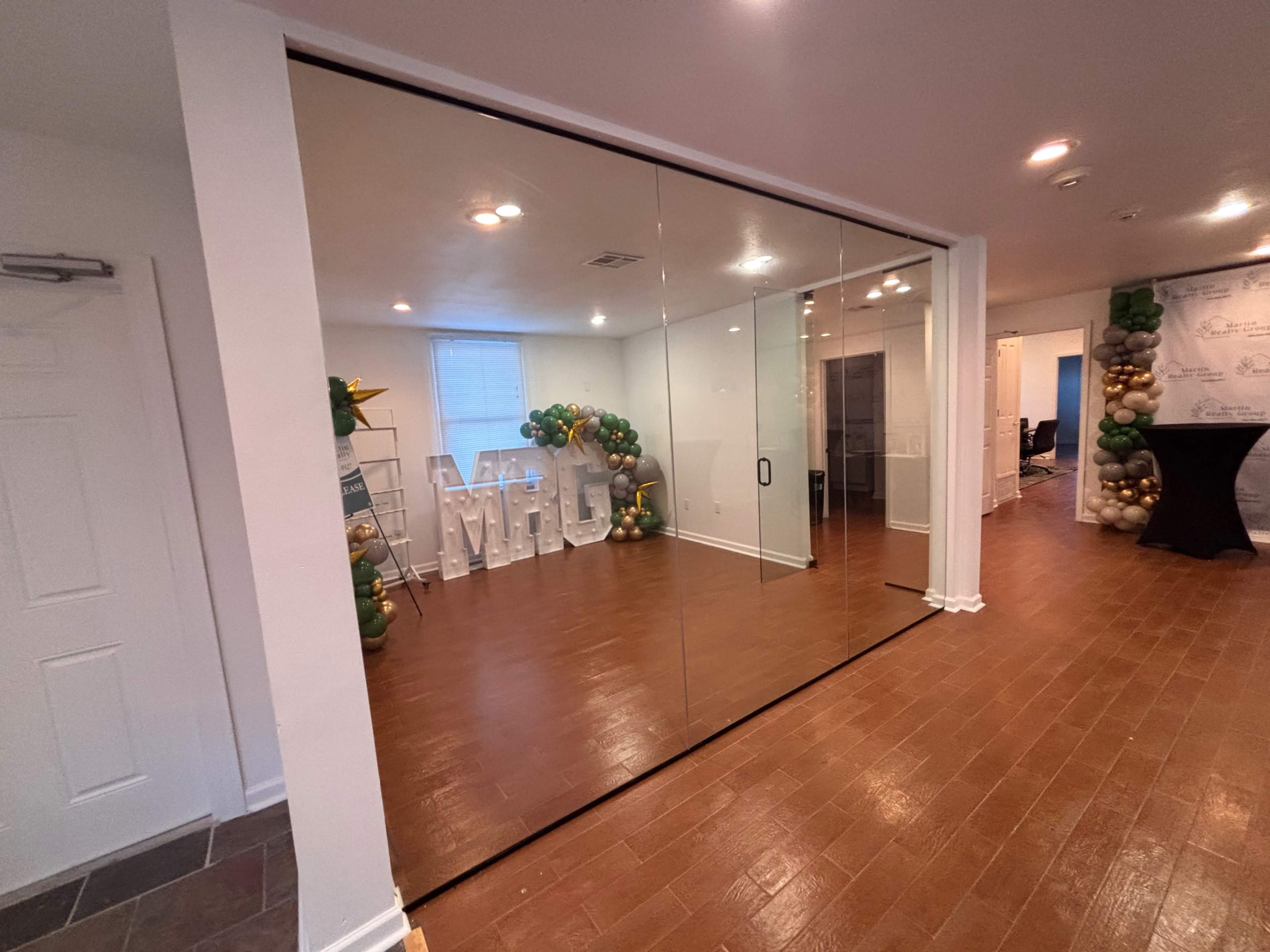 A glass wall separates two rooms, with large letters spelling "MHC" displayed in one area and a balloon arch in the other.