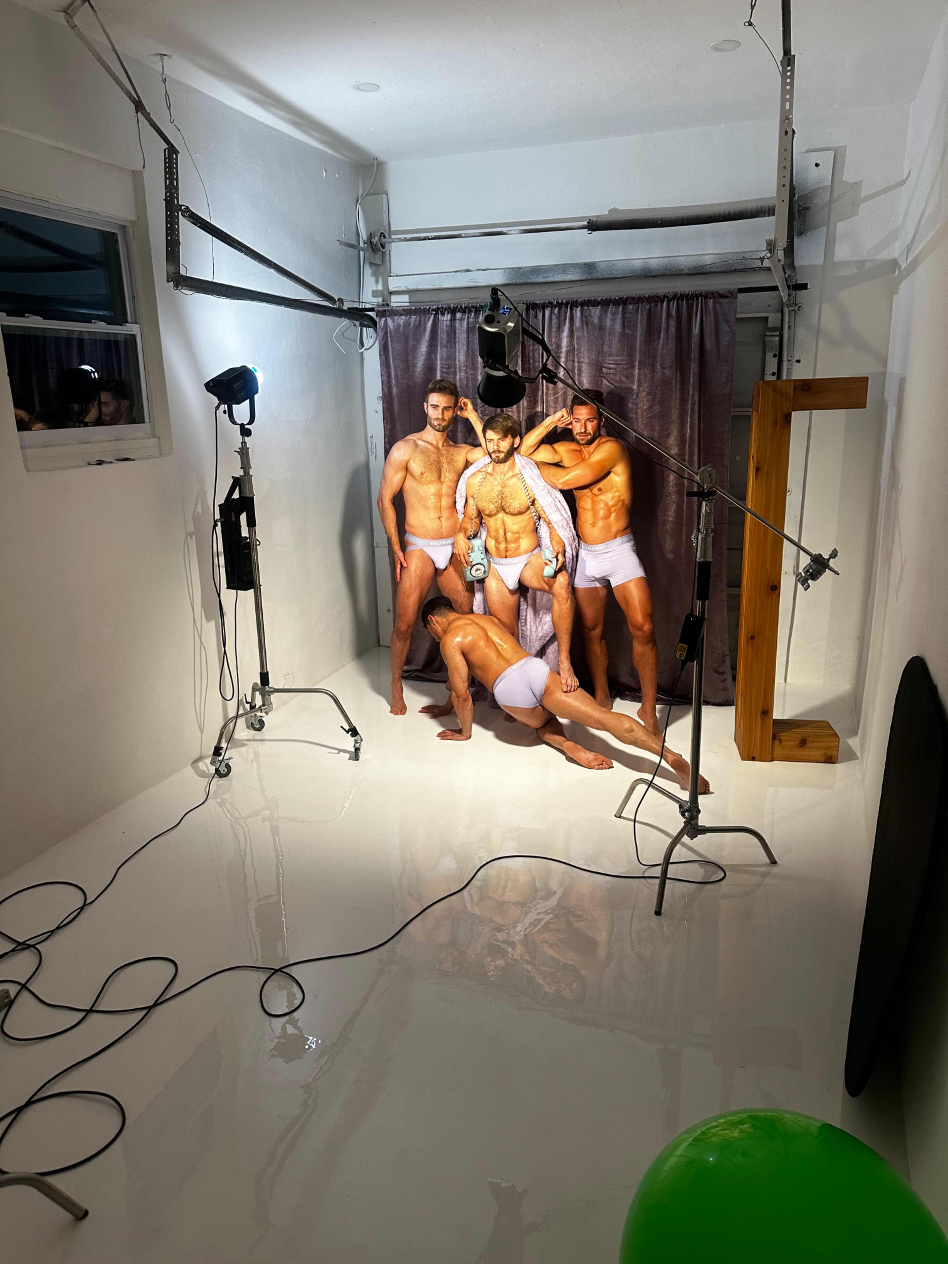 A group of four male models poses in a studio setting with bright lighting and a glossy white floor.