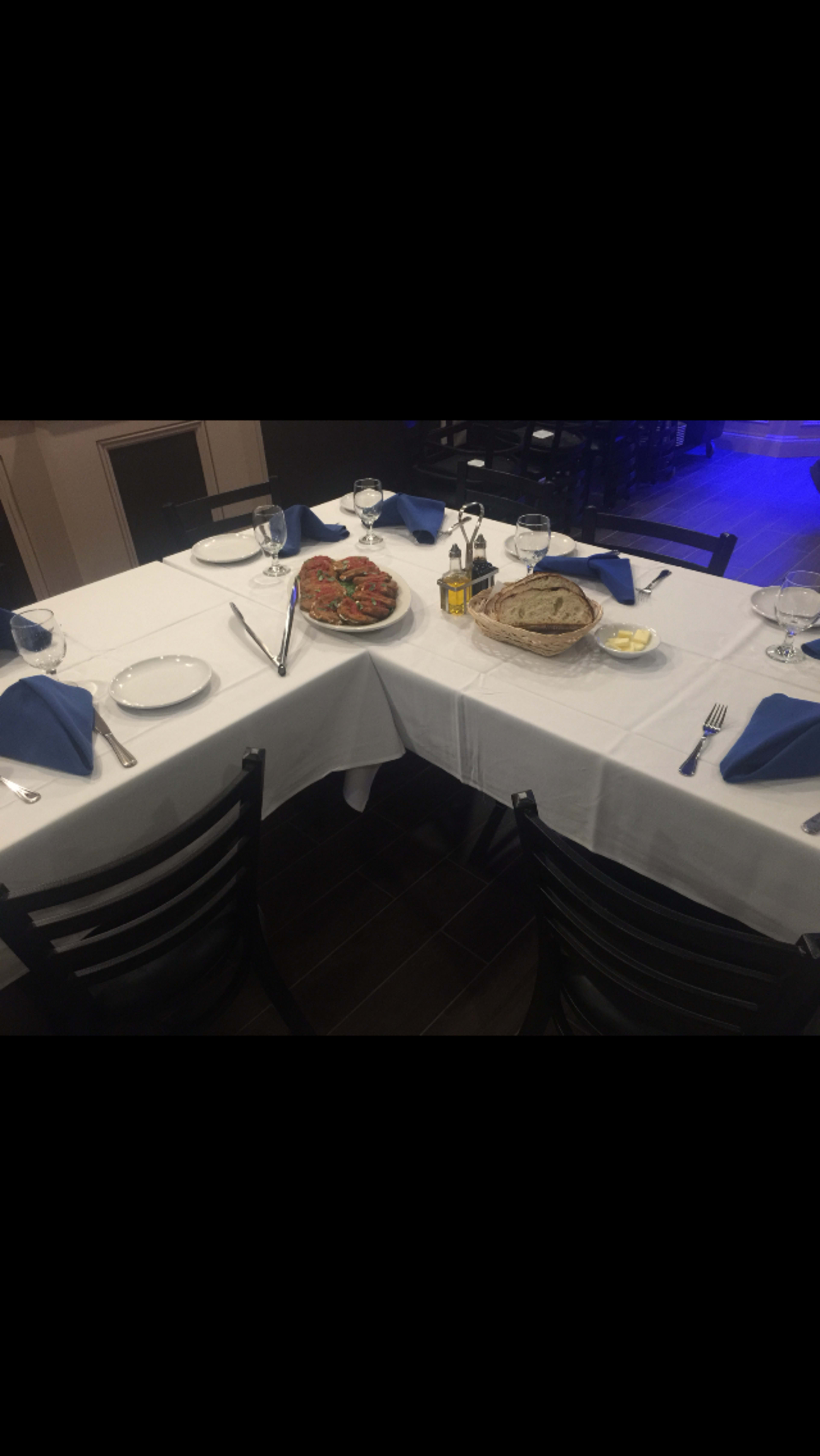A dining table is set with white tablecloths, blue napkins, plates, glasses, and two baskets containing food items.