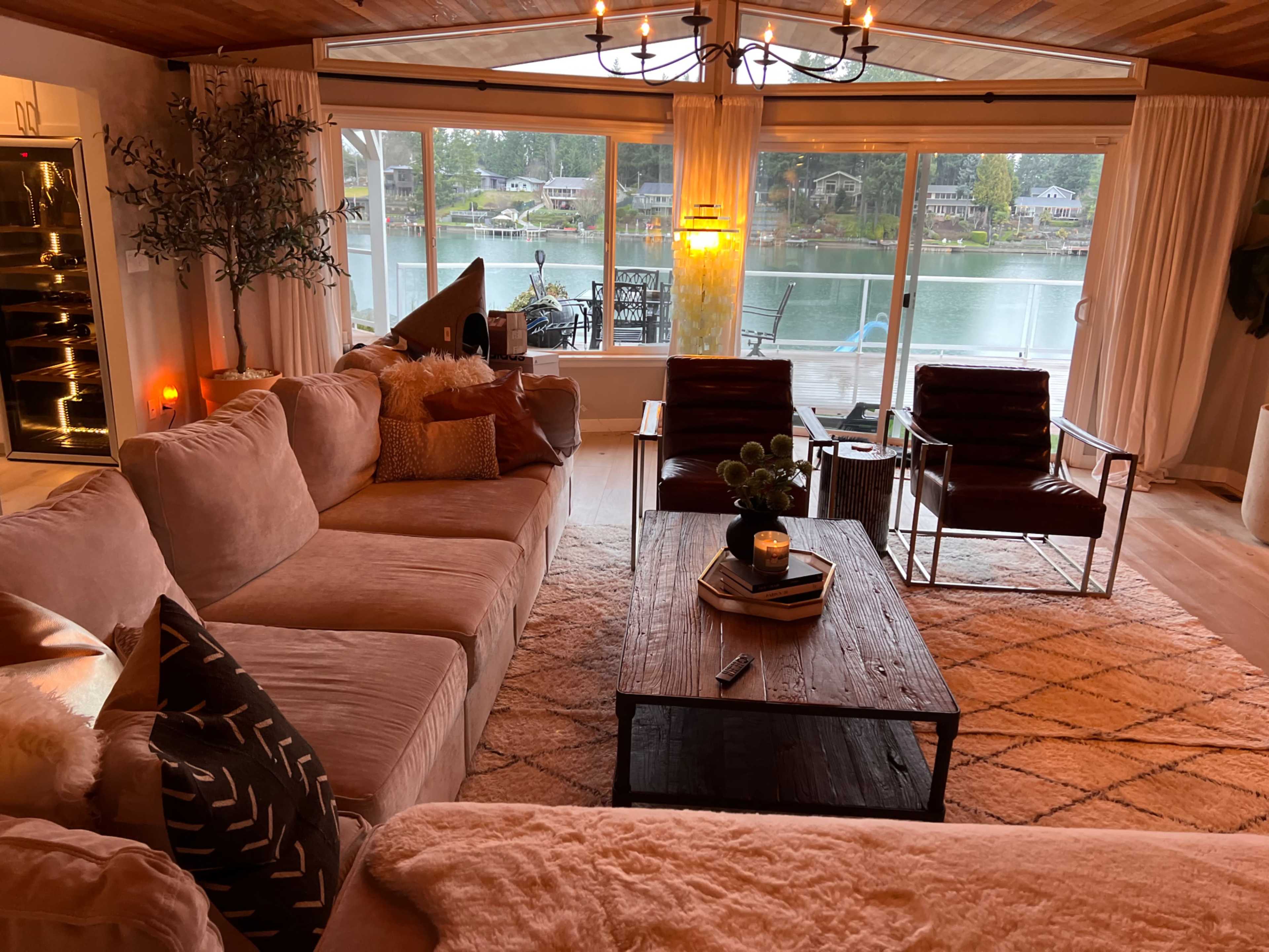 The living room features a large sectional couch, a wooden coffee table, and a view of a lake through large windows.