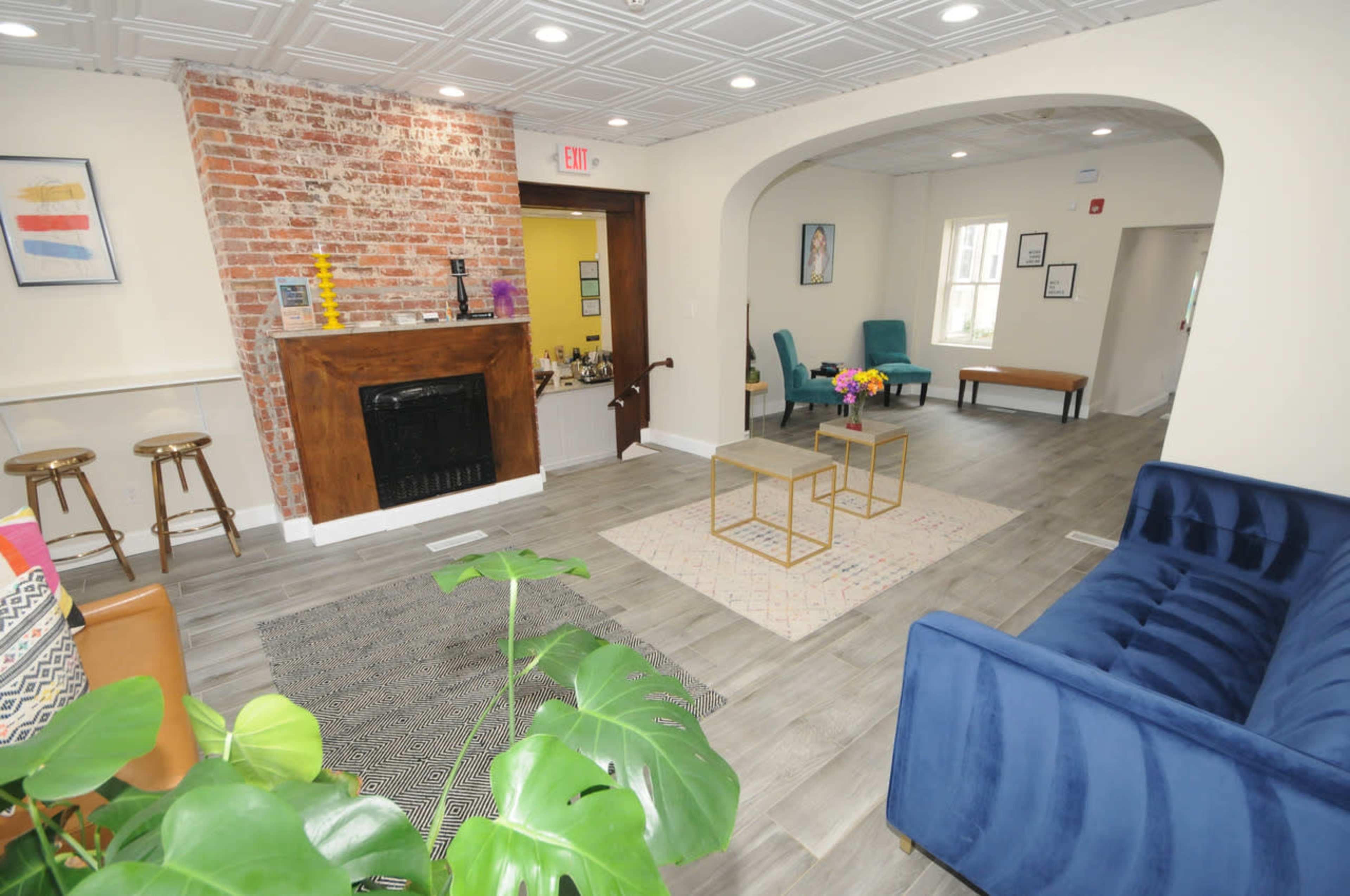 The image shows a welcoming lounge area featuring a blue sofa, a wooden bar with stools, and a seating arrangement with colorful chairs and a coffee table.