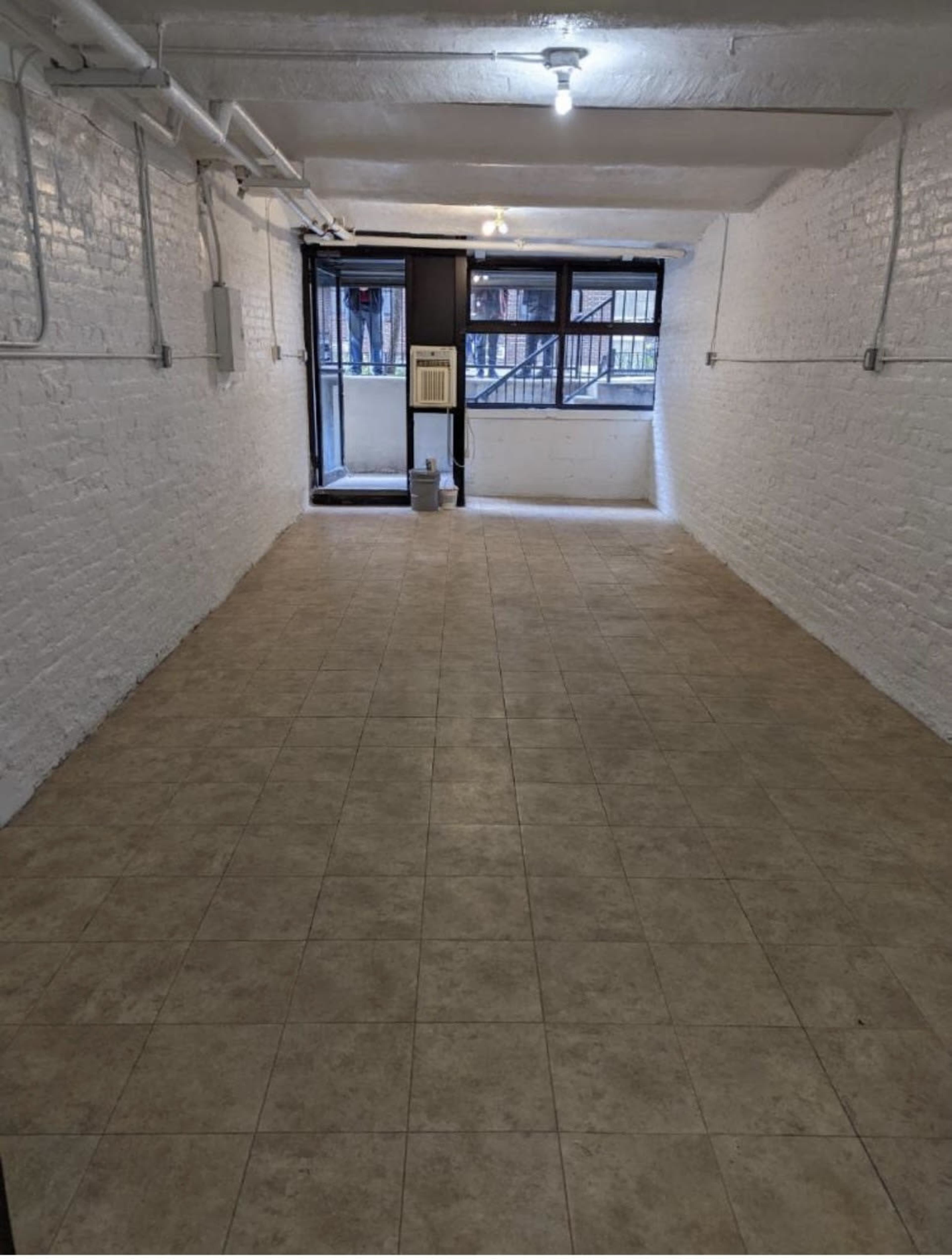 A large, empty basement space with tiled flooring and a door leading to the outside.