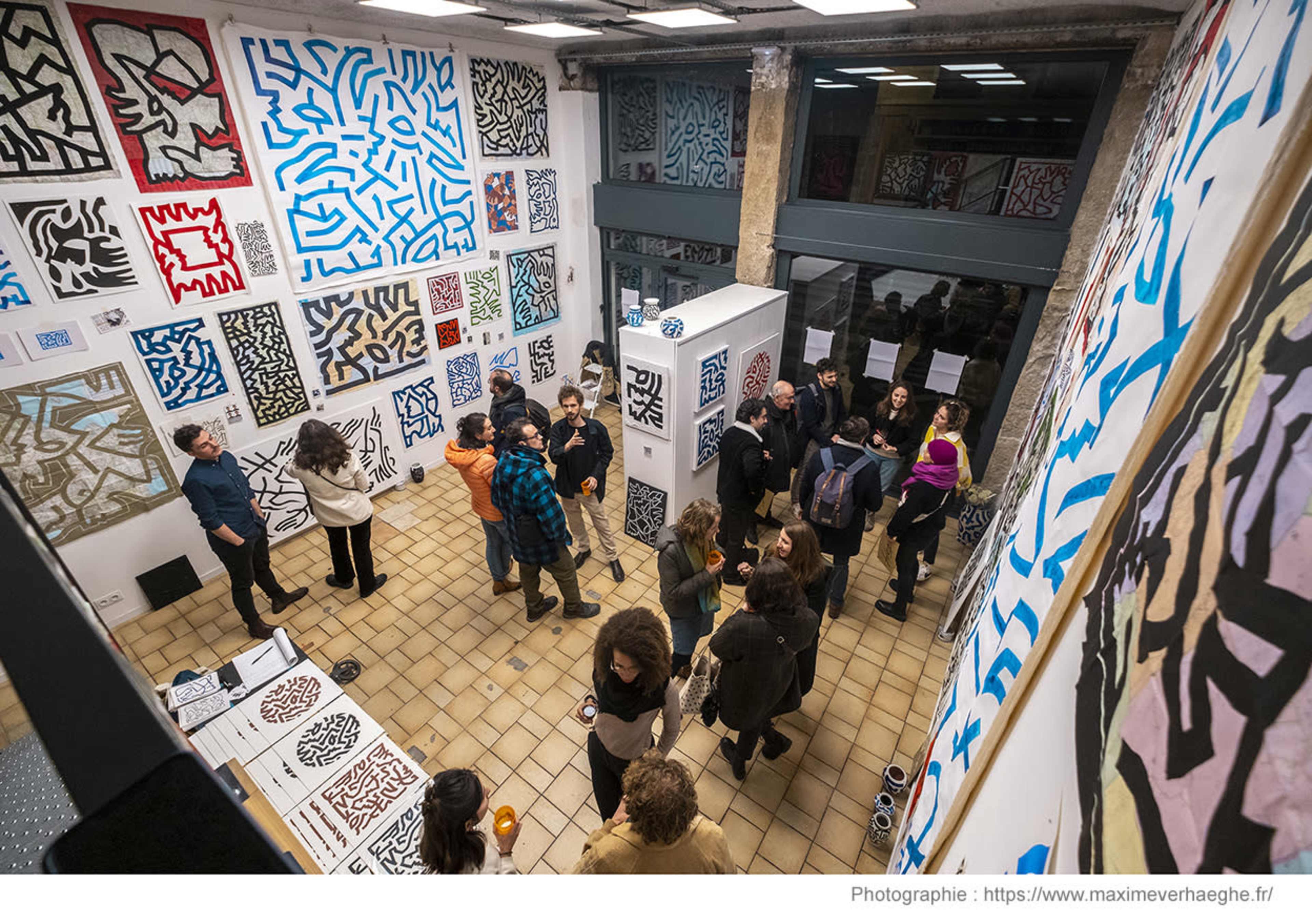 A group of people gather in an art gallery surrounded by colorful abstract artworks on the walls.