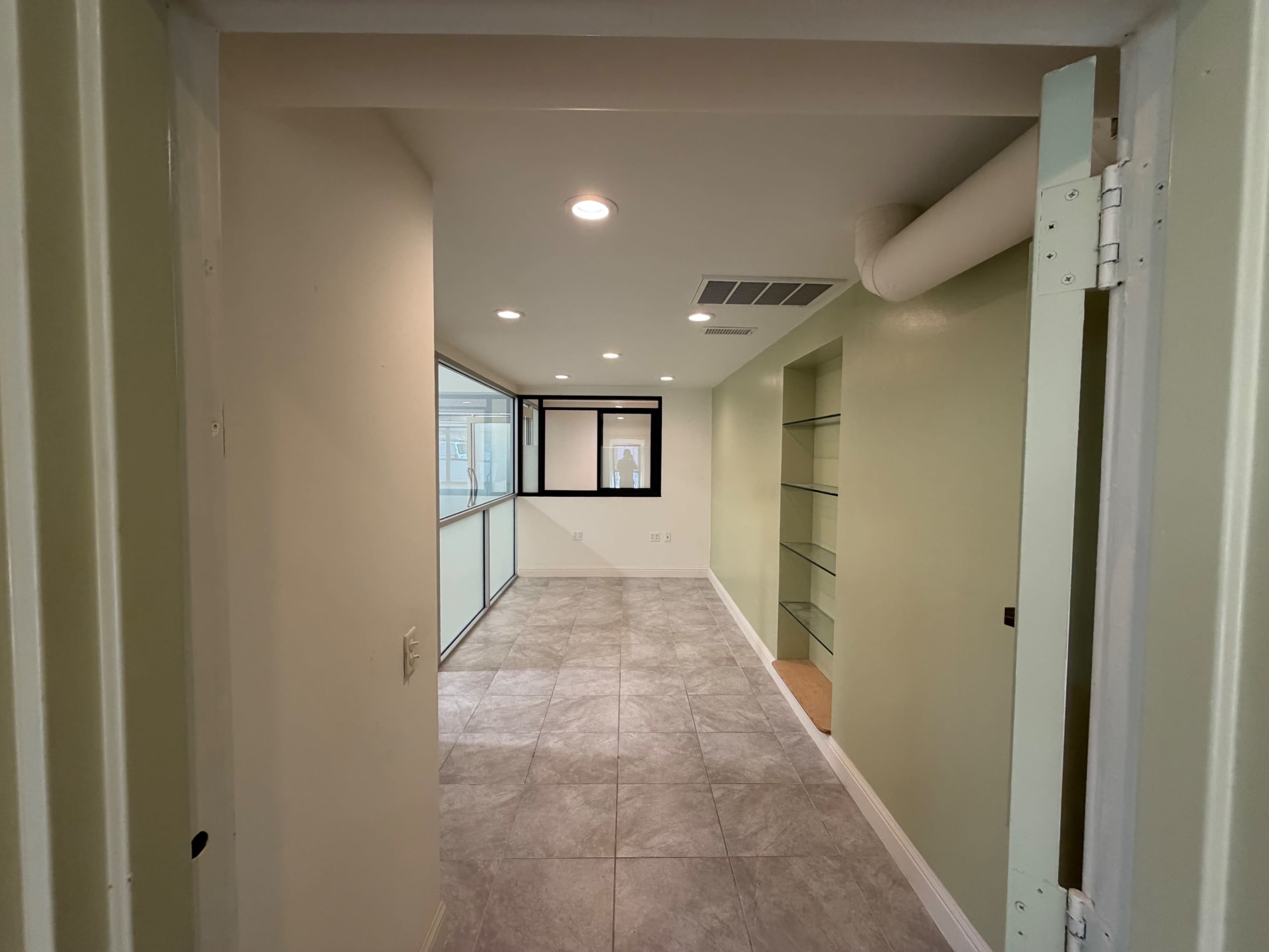 The image shows a well-lit, empty room with tiled flooring, green walls, and a large window along one side.