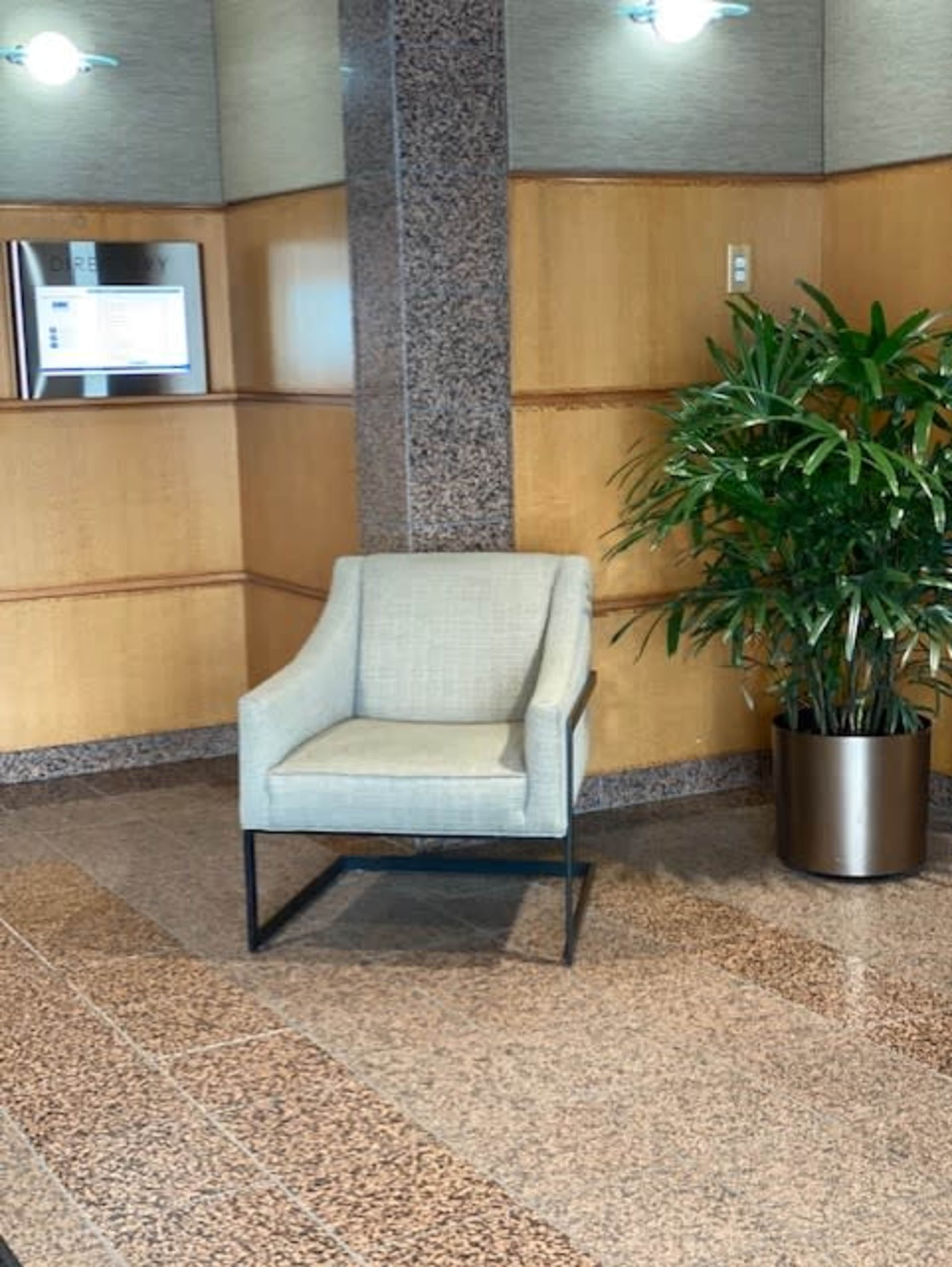 A single beige chair next to a potted plant in a lobby area with wooden and granite walls.