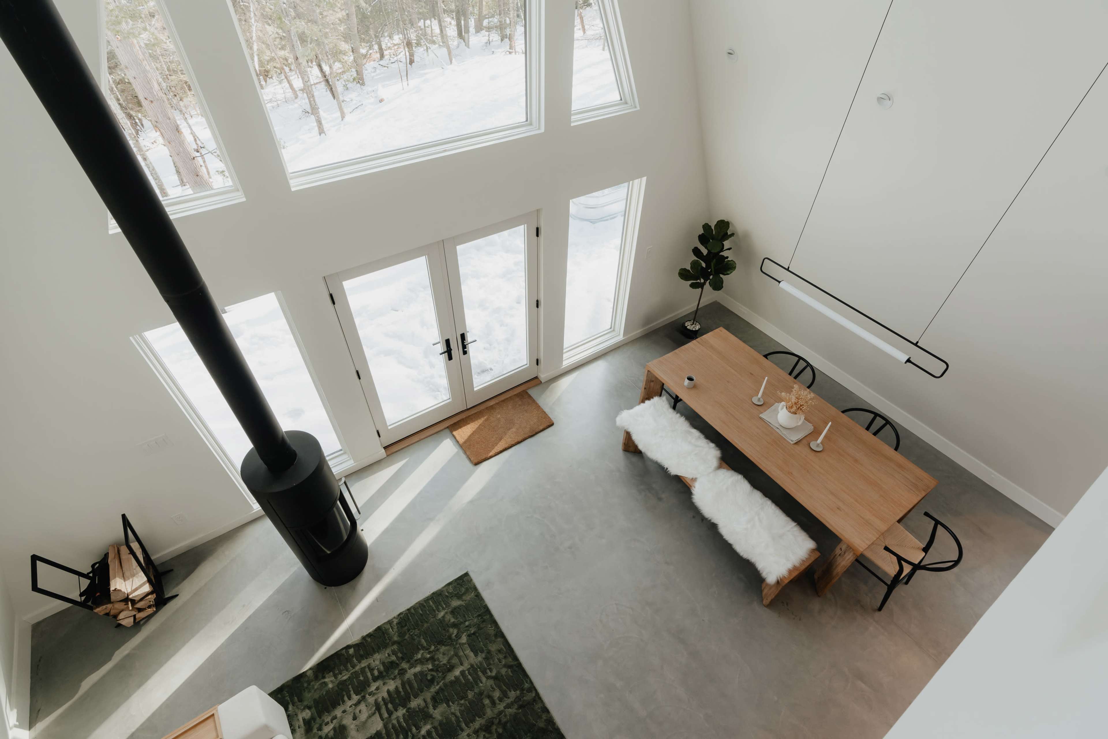 A modern, open-concept dining area with a large wooden table, black chairs, and a floor-to-ceiling window overlooking a snowy landscape.