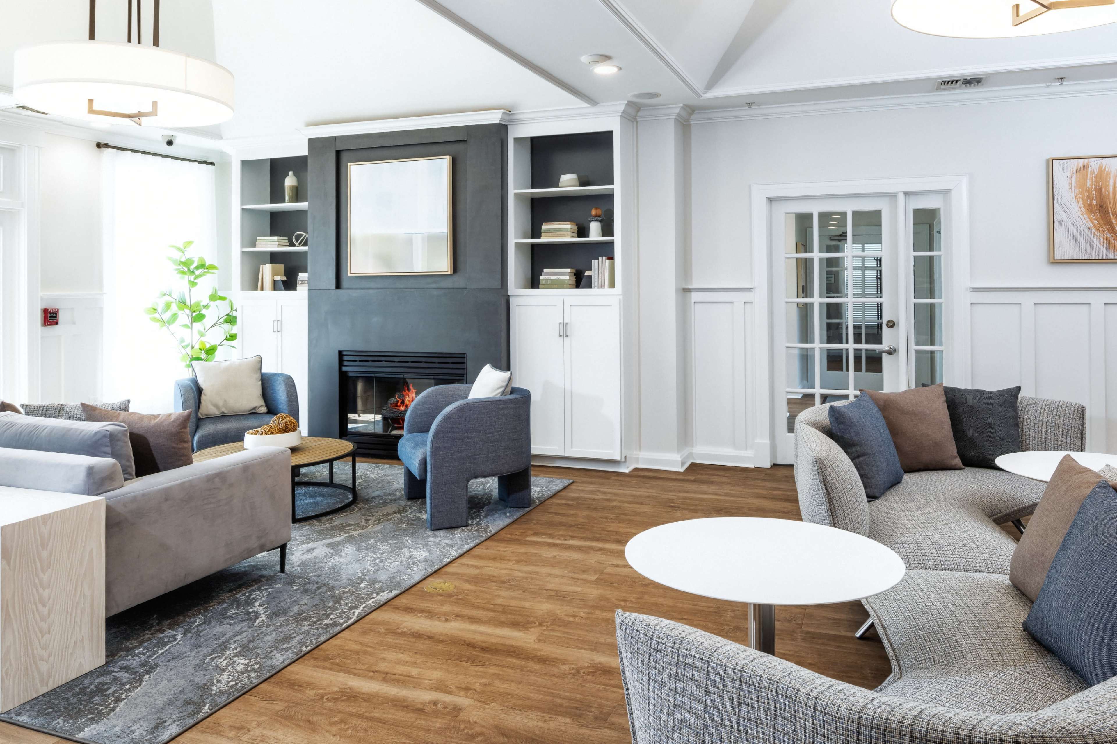 A modern living room with gray sofas, a fireplace, built-in shelves, and circular tables on a hardwood floor.