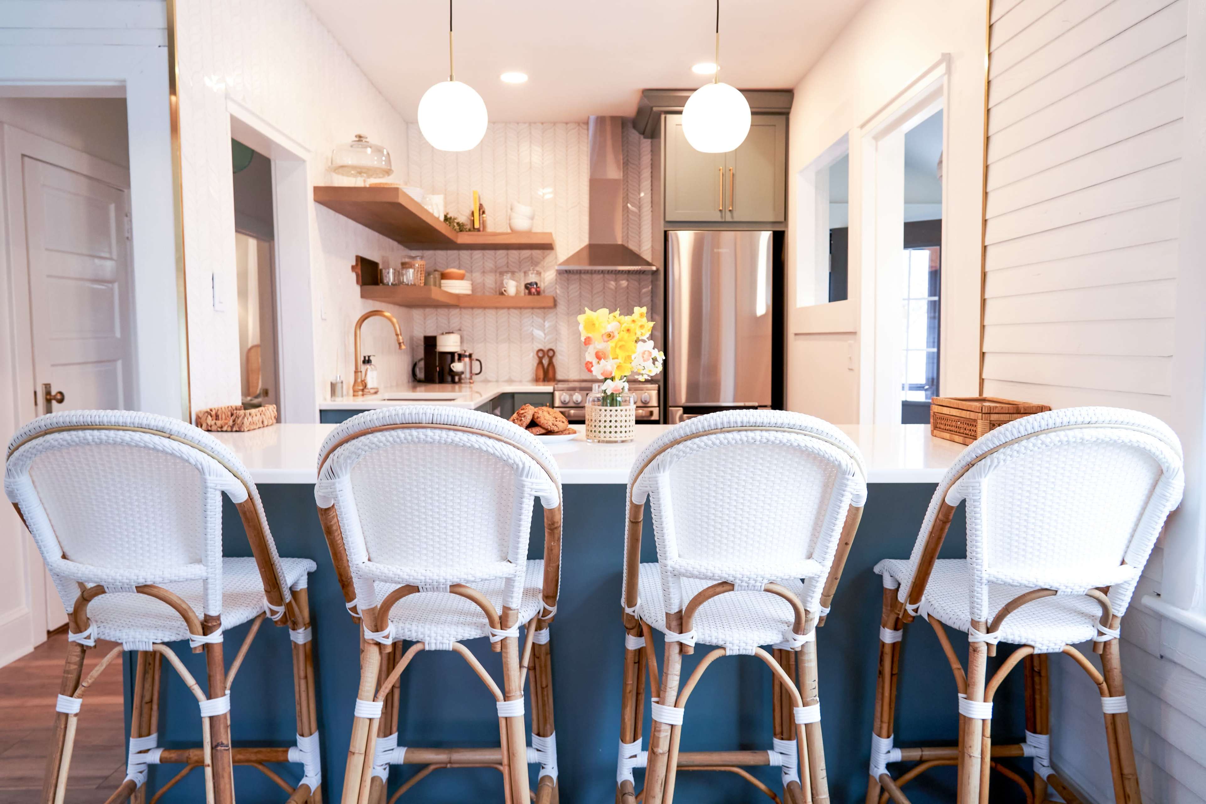A modern kitchen features a long island with four wicker bar stools, complemented by a well-organized countertop and stylish decor.