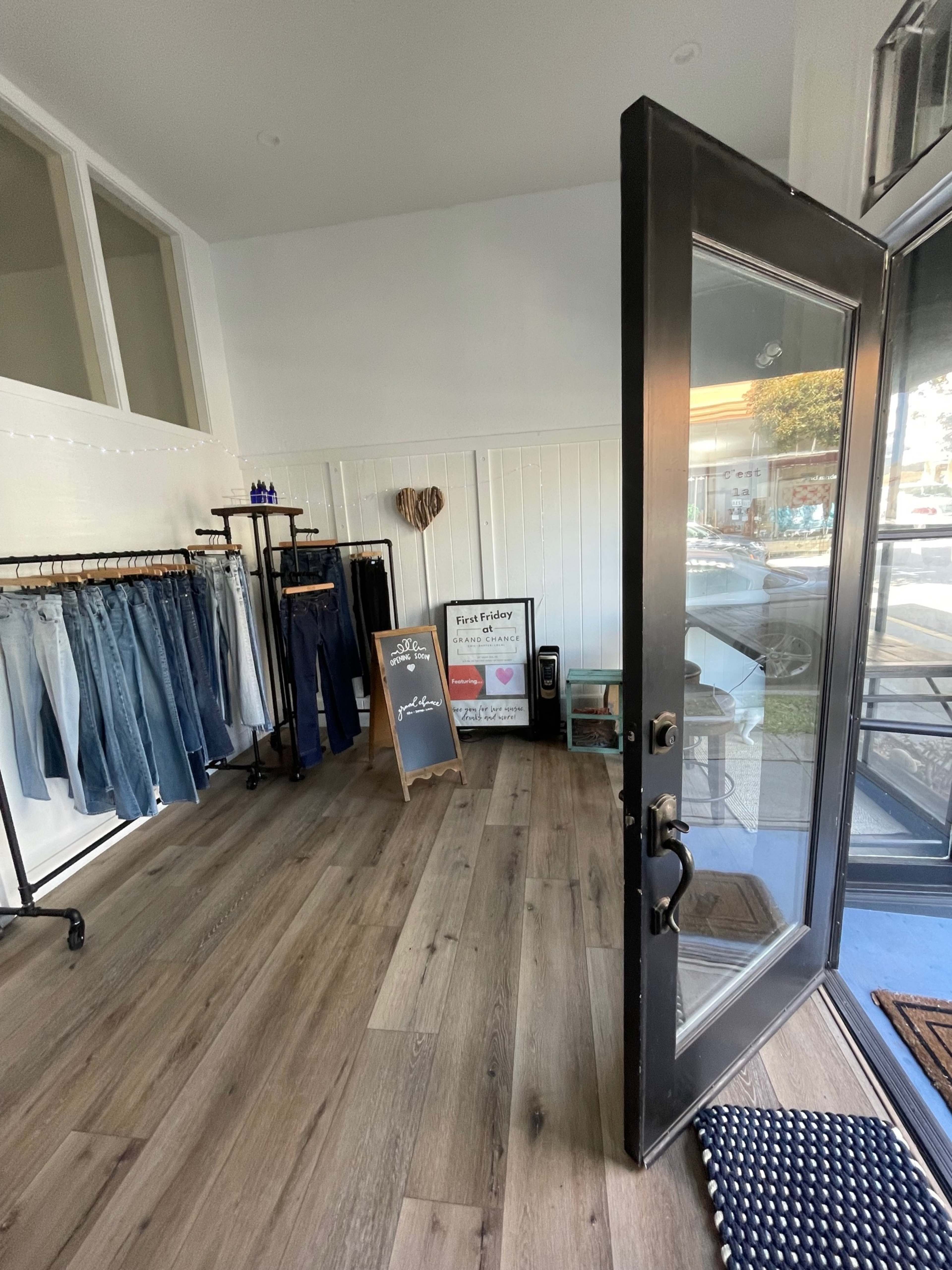 A retail space features hanging denim on racks, a promotional chalkboard, and an entrance door leading to the street outside.