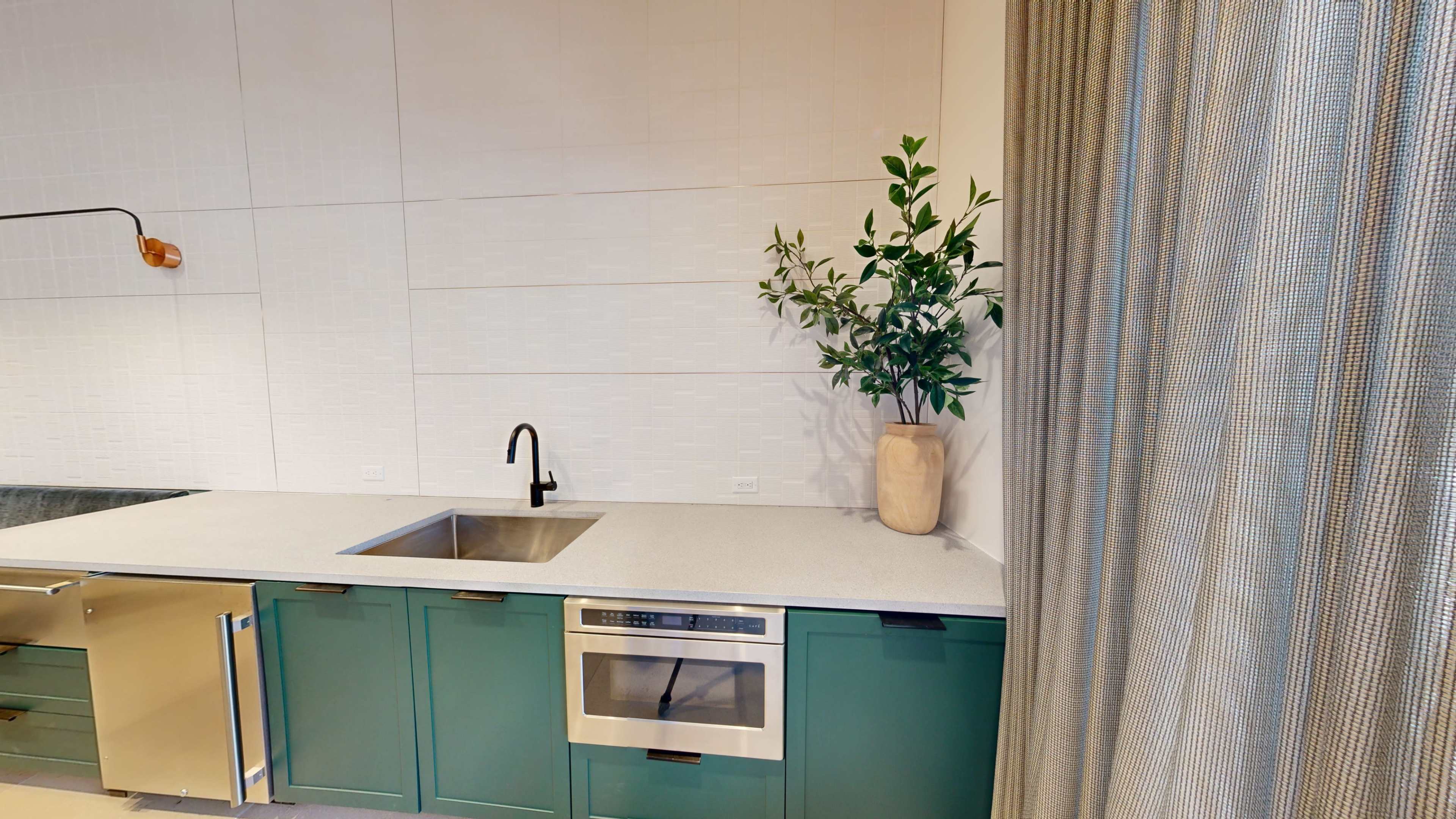 A kitchen corner features a green cabinet underneath a countertop with a sink and built-in microwave, complemented by a vase of greenery.