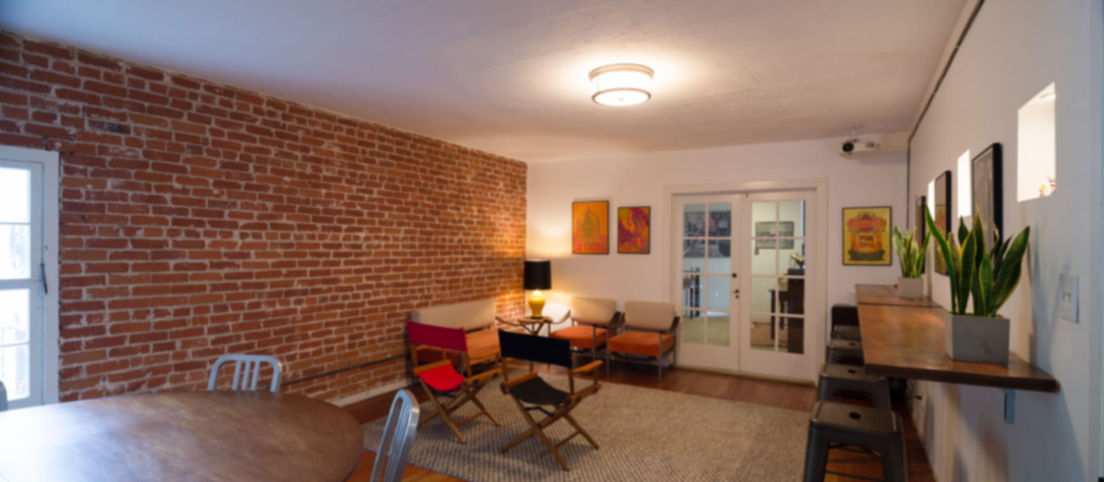 The image shows a well-lit living space featuring a brick wall, various seating options, and a round dining table.