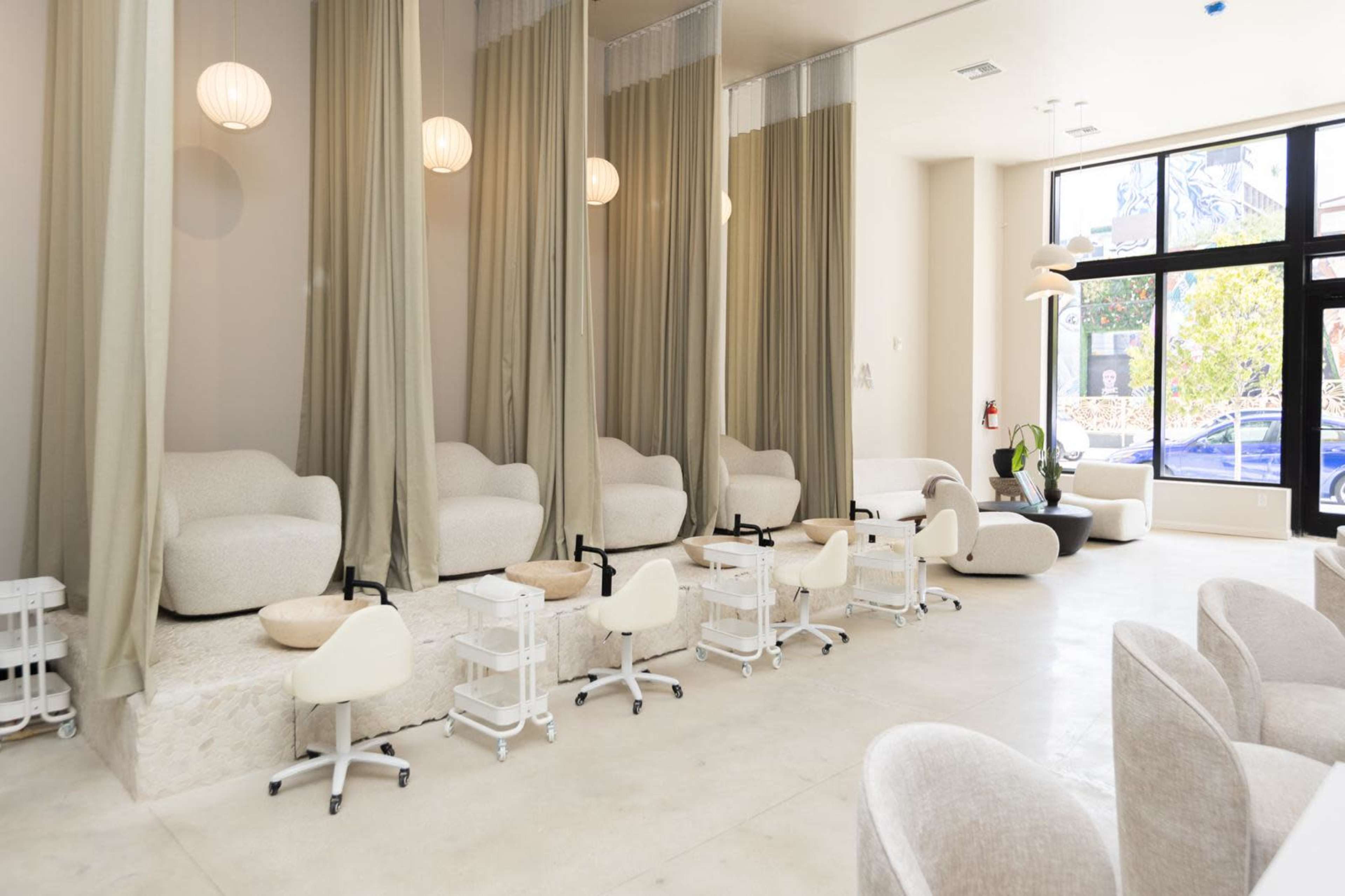 The image shows a modern salon interior with several pedicure stations featuring cushioned chairs, footbaths, and curtains for privacy.