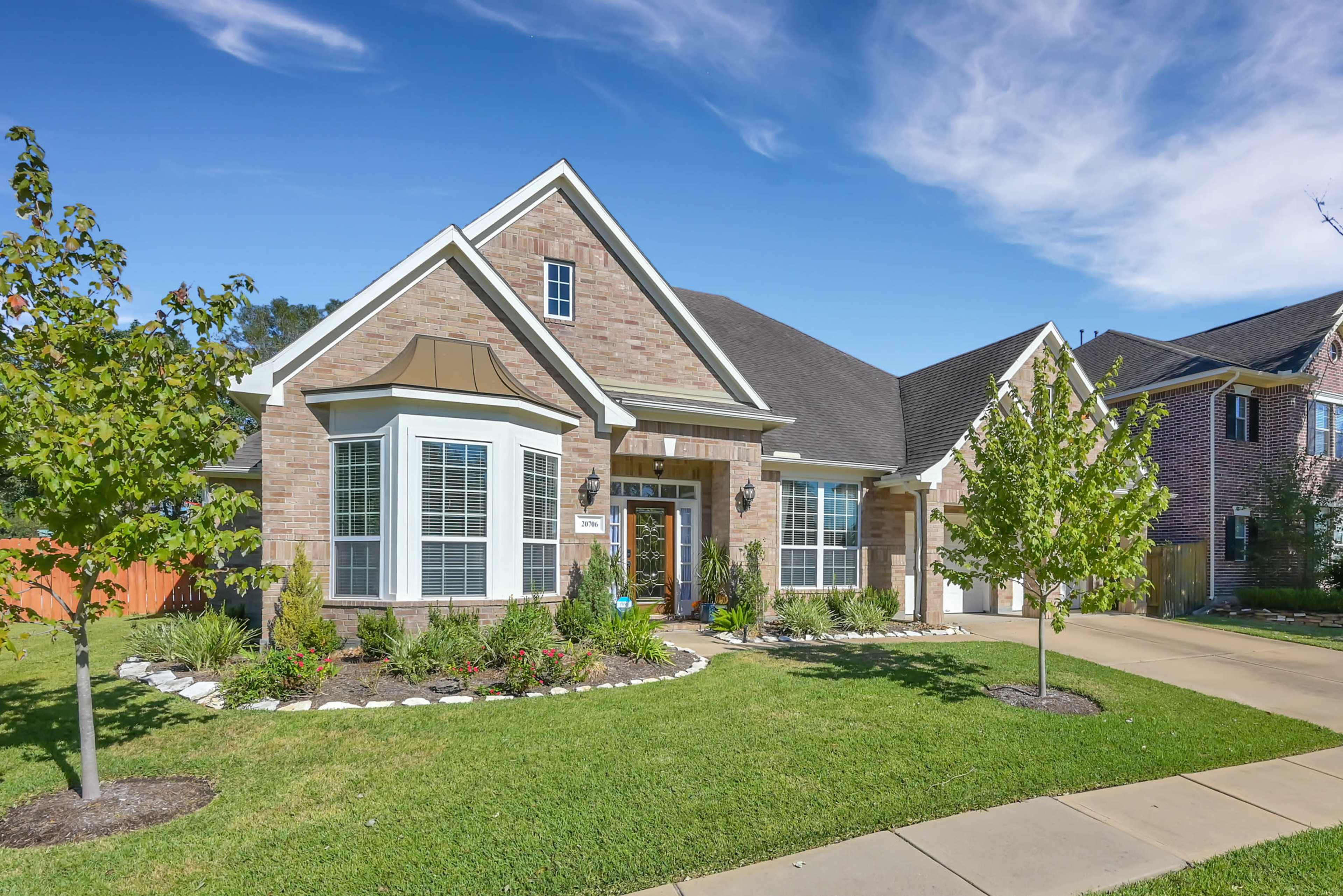 A brick house with a peaked roof and landscaped front yard sits on a quiet residential street.