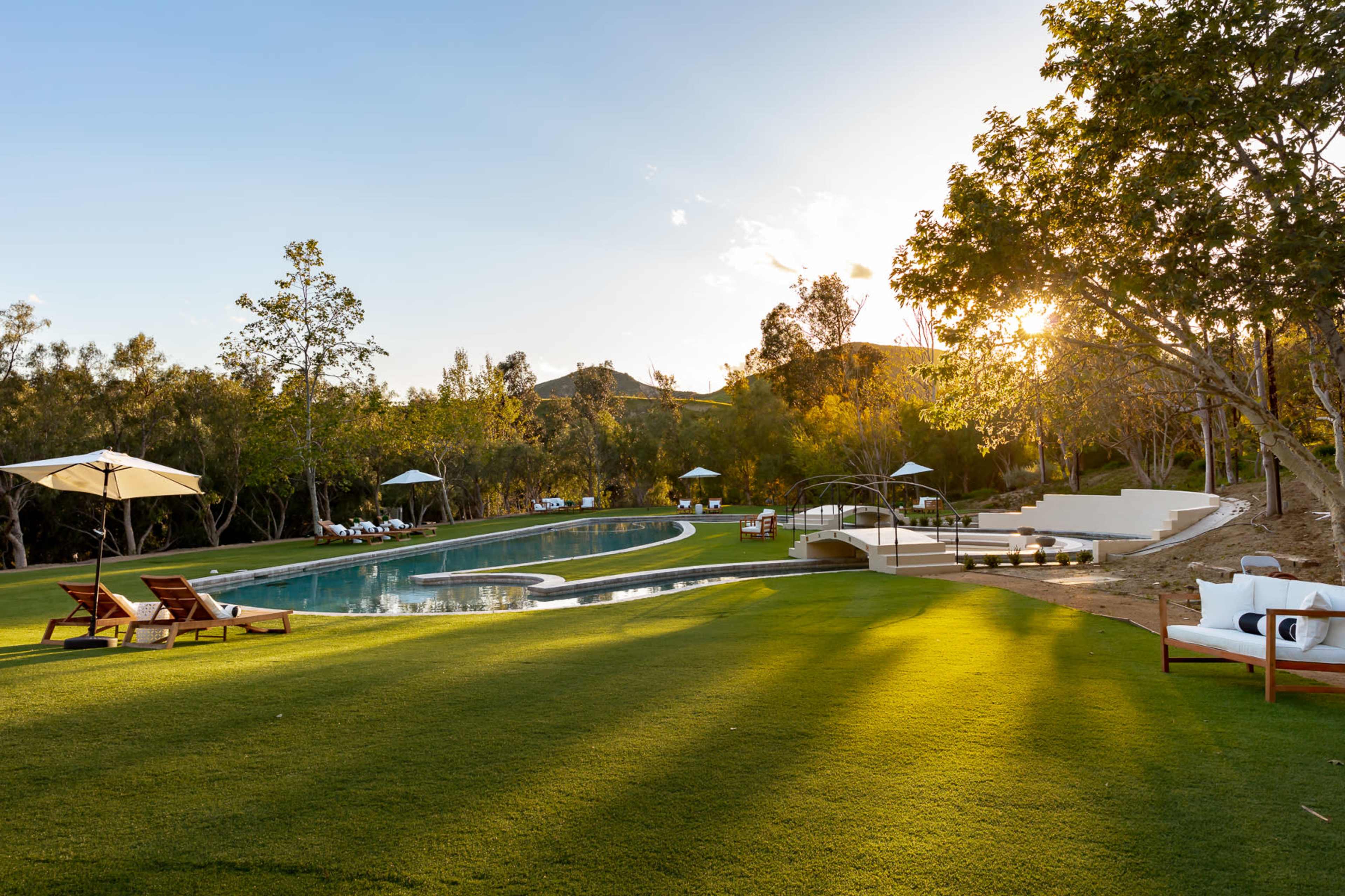 A landscaped outdoor area featuring a swimming pool, lounge chairs, and trees, with sunlight filtering through the foliage.