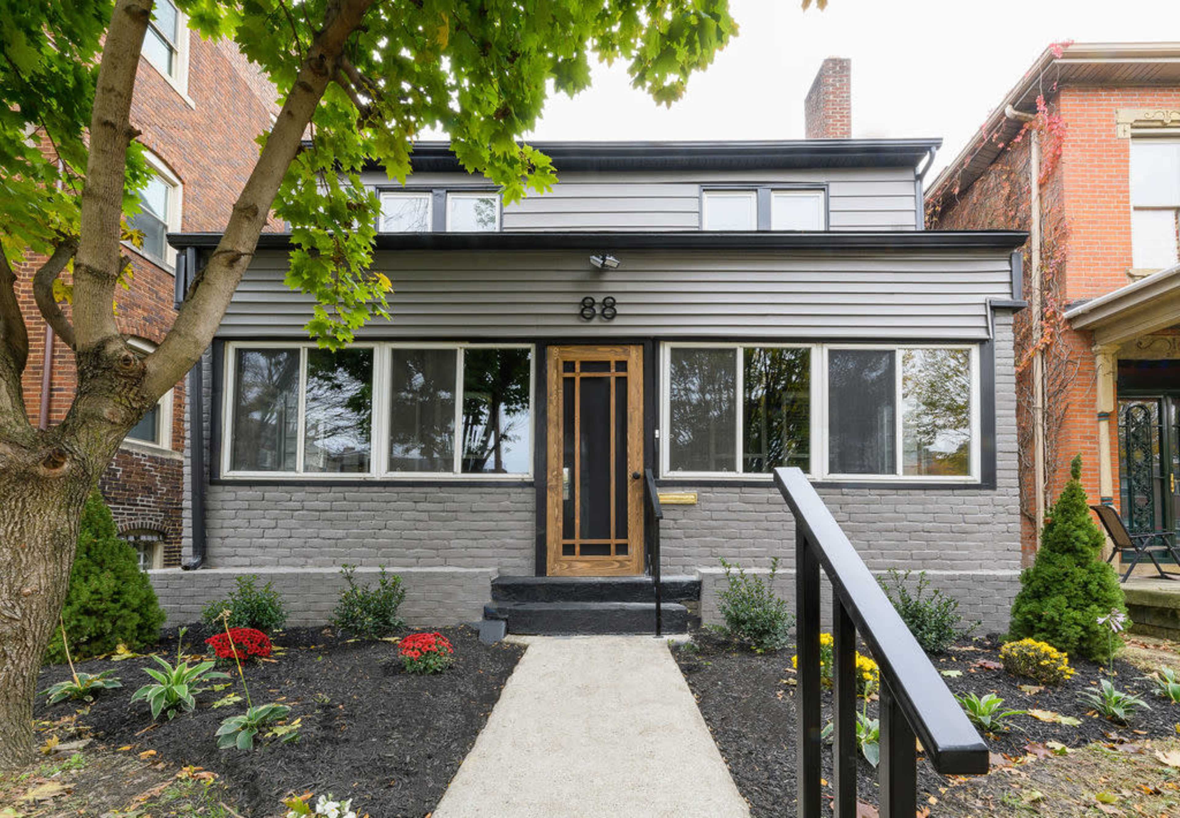 A two-story house with a gray exterior, large front windows, and a small landscaped pathway leading to the entrance.