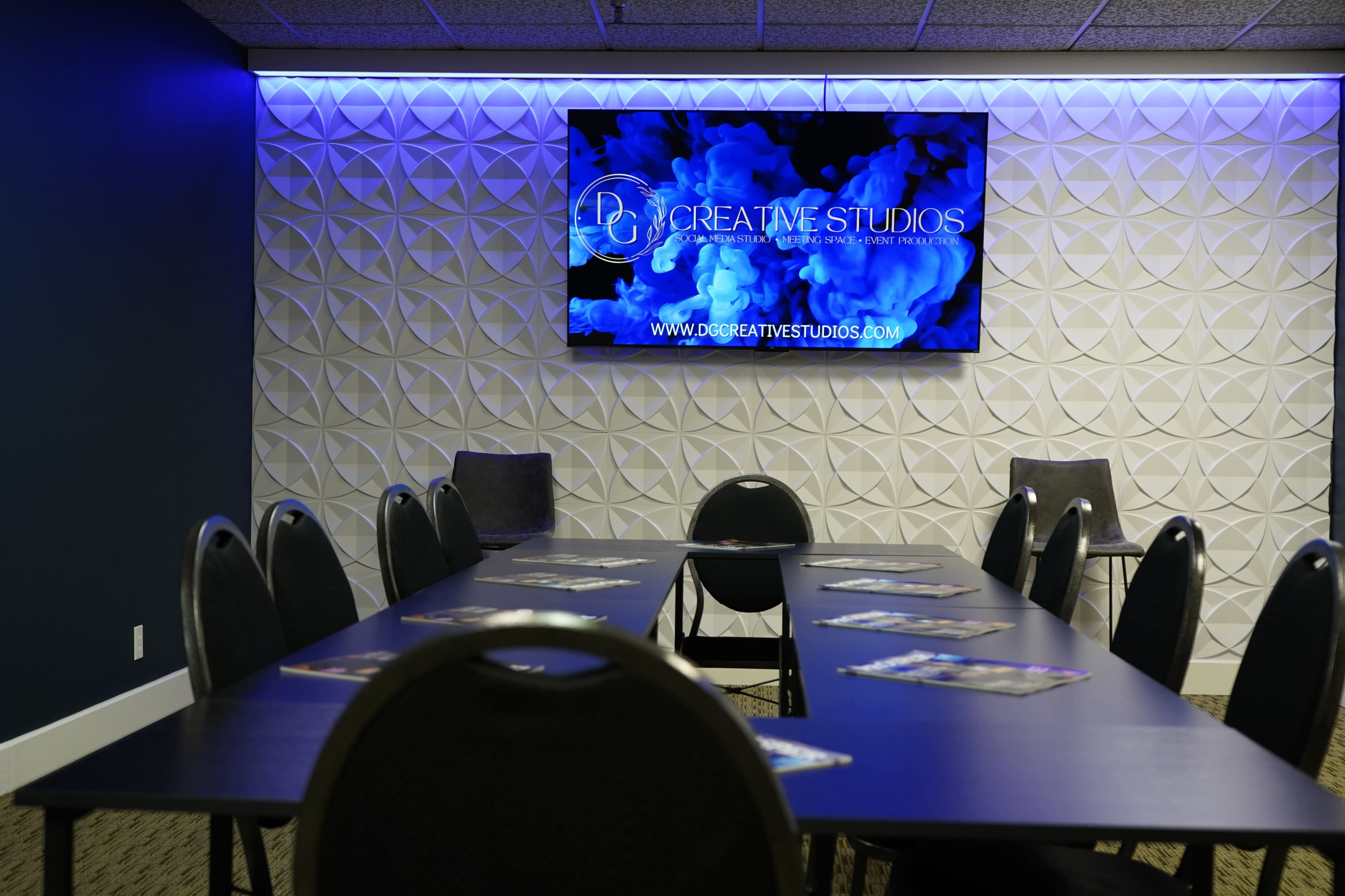 A conference room features a long table with chairs, illuminated by blue lighting, and a screen displaying the logo of D7 Creative Studios on the wall.
