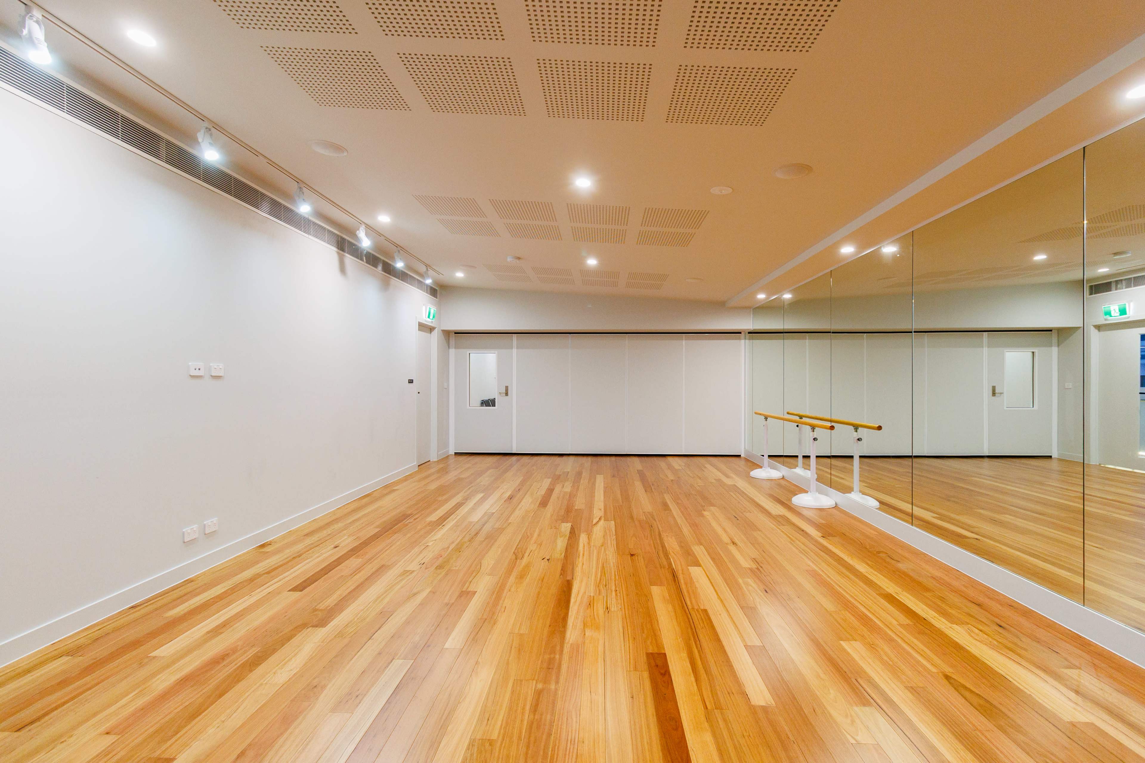 The image shows a spacious, well-lit dance studio featuring a mirrored wall, wooden flooring, and a ballet barre.