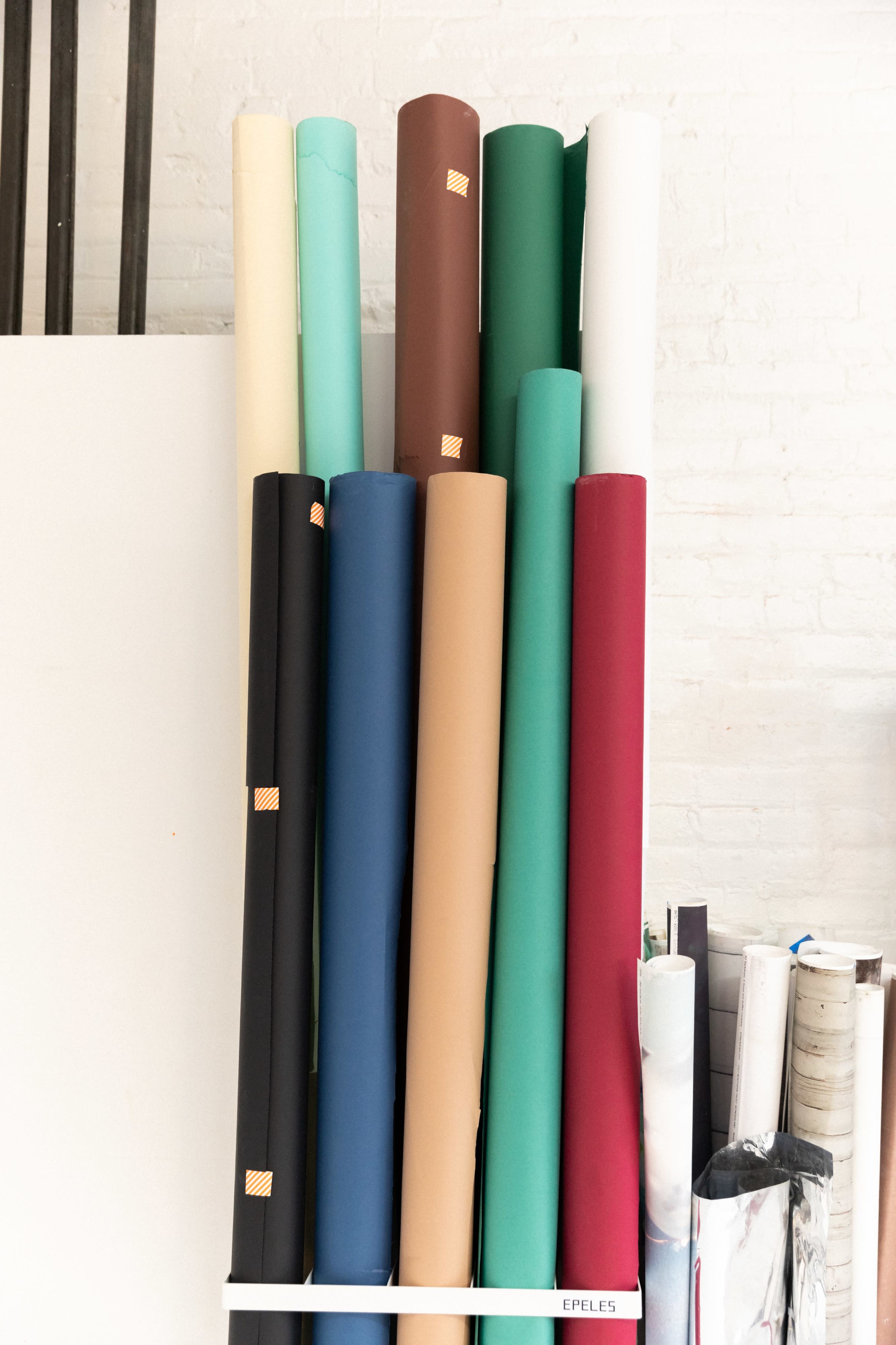 A collection of neatly stacked and rolled sheets of paper in various colors is displayed against a white wall.