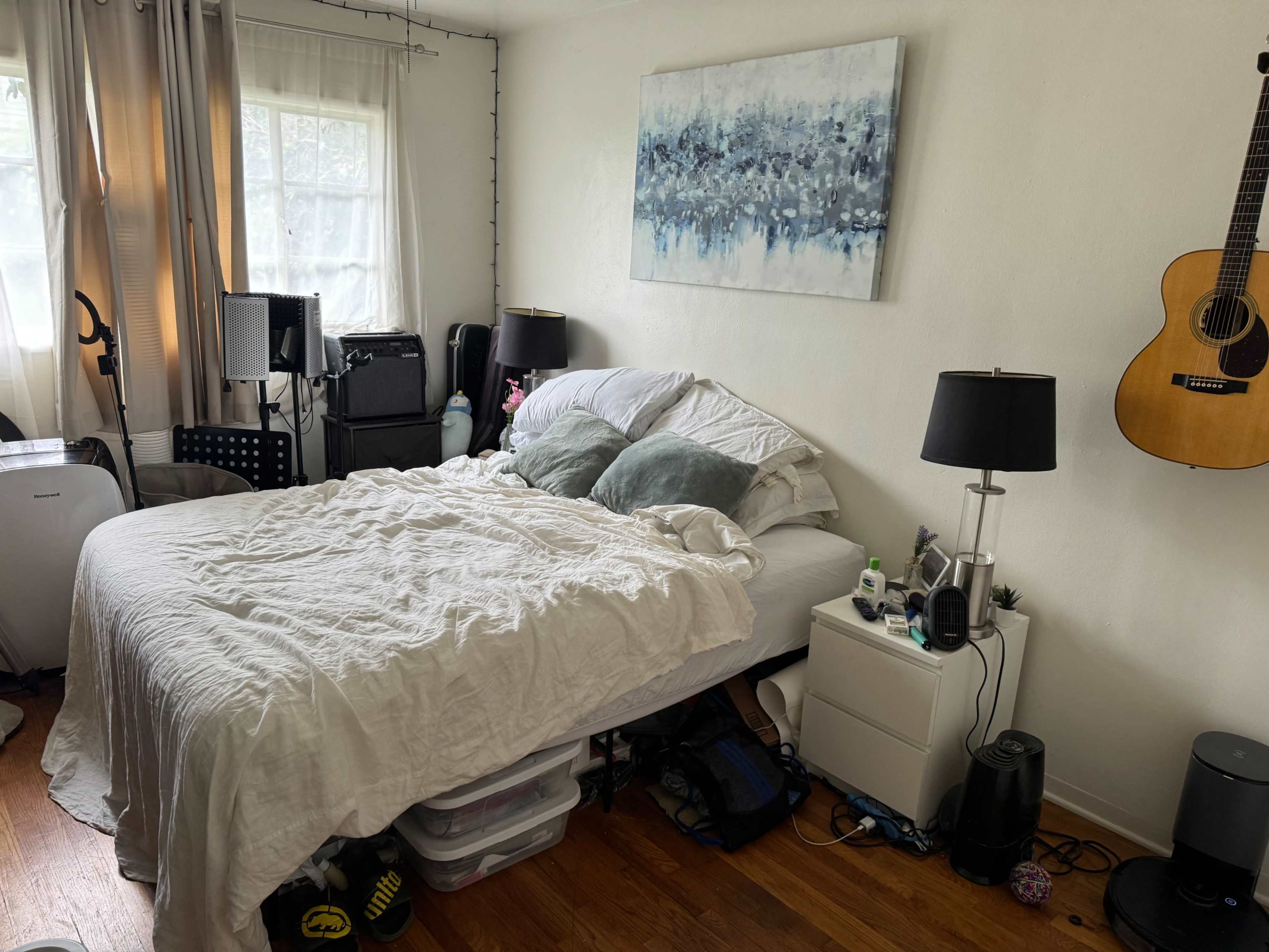 The image shows a bedroom with a bed, bedside tables, an acoustic guitar on the wall, and various items scattered around the floor.