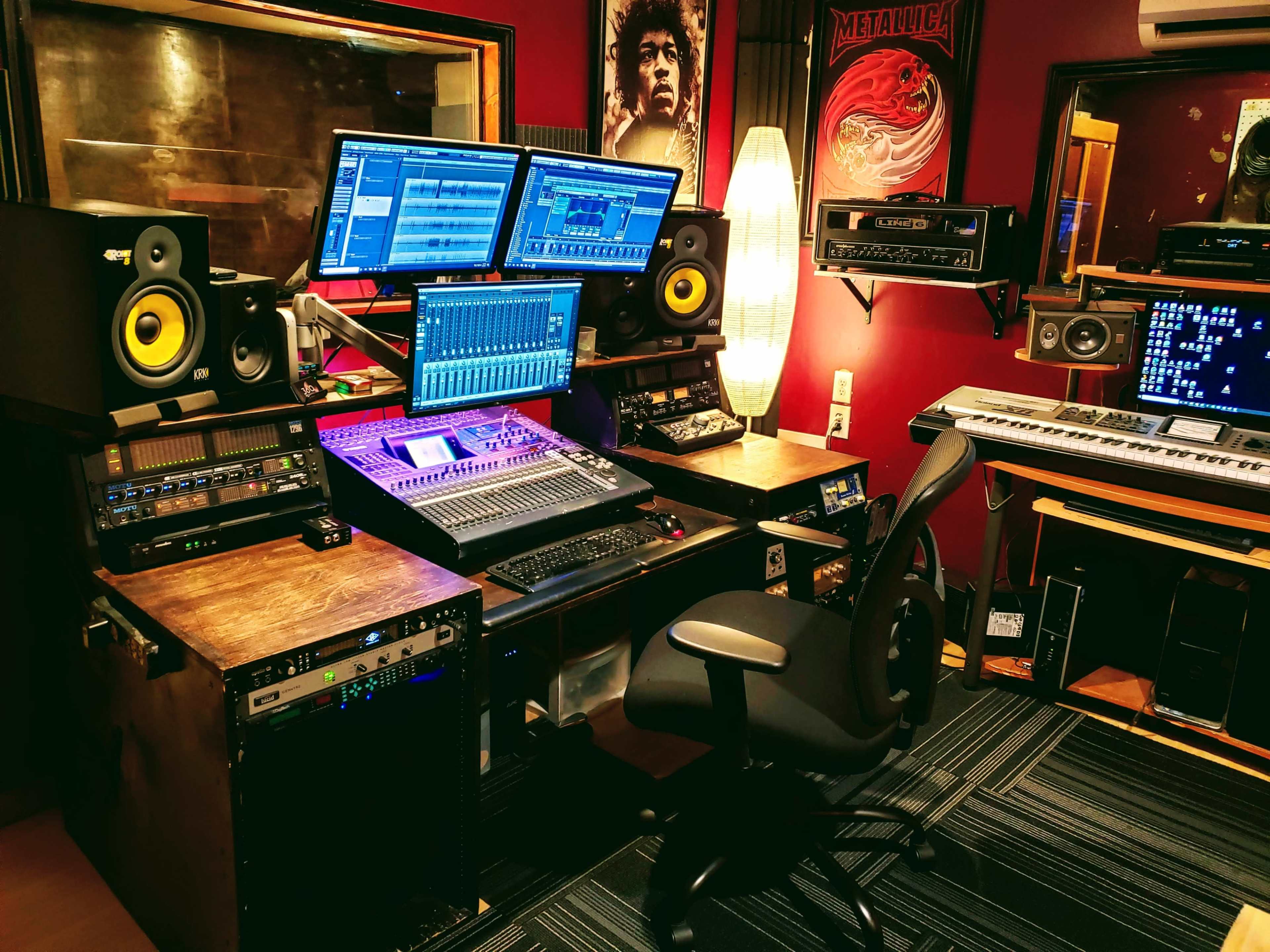 A music production studio with multiple screens, audio equipment, and a swivel chair arranged around a central mixing console.