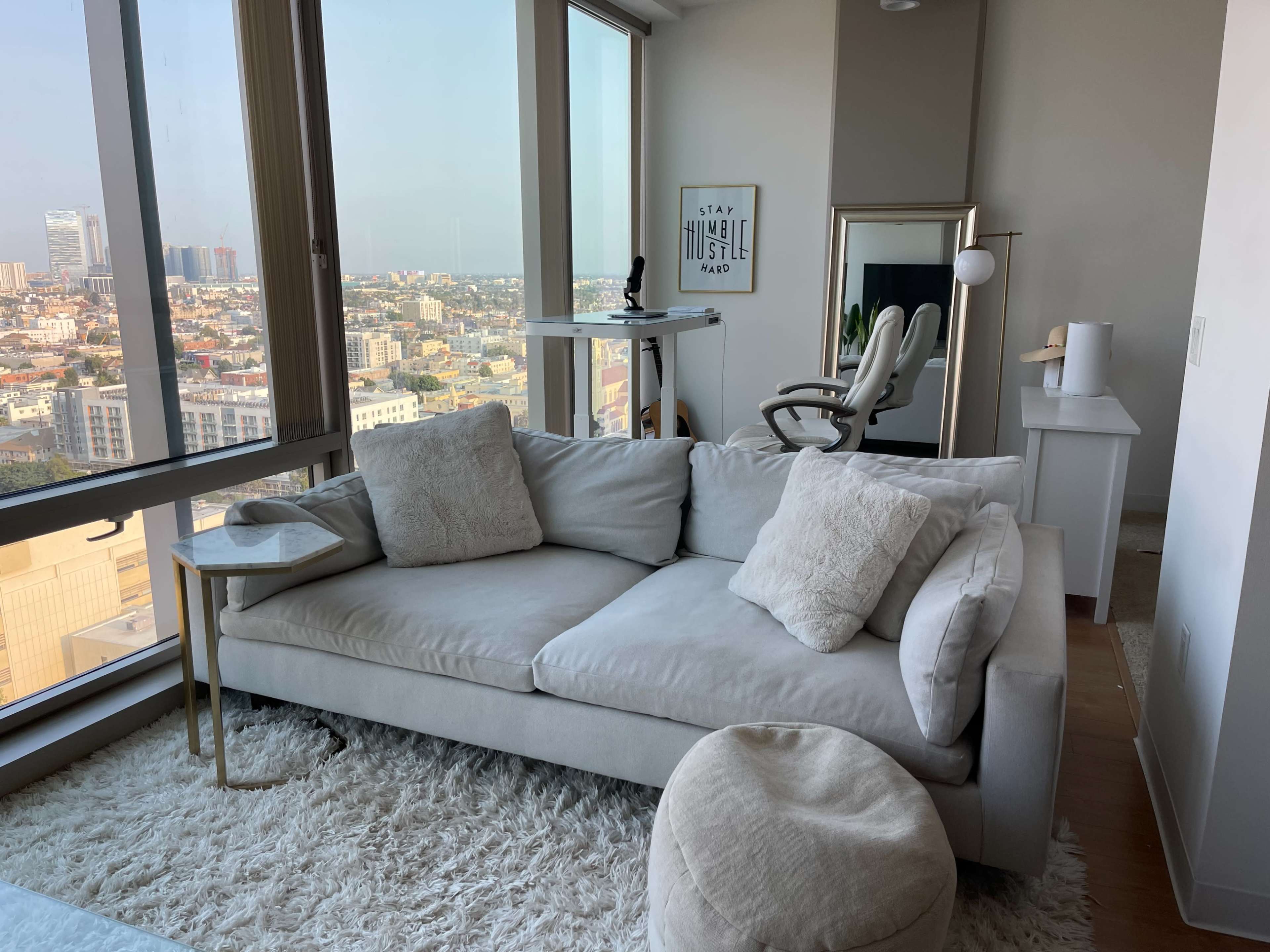 A modern living room features a light-colored sofa, a small side table, and a view of a city skyline through large windows.