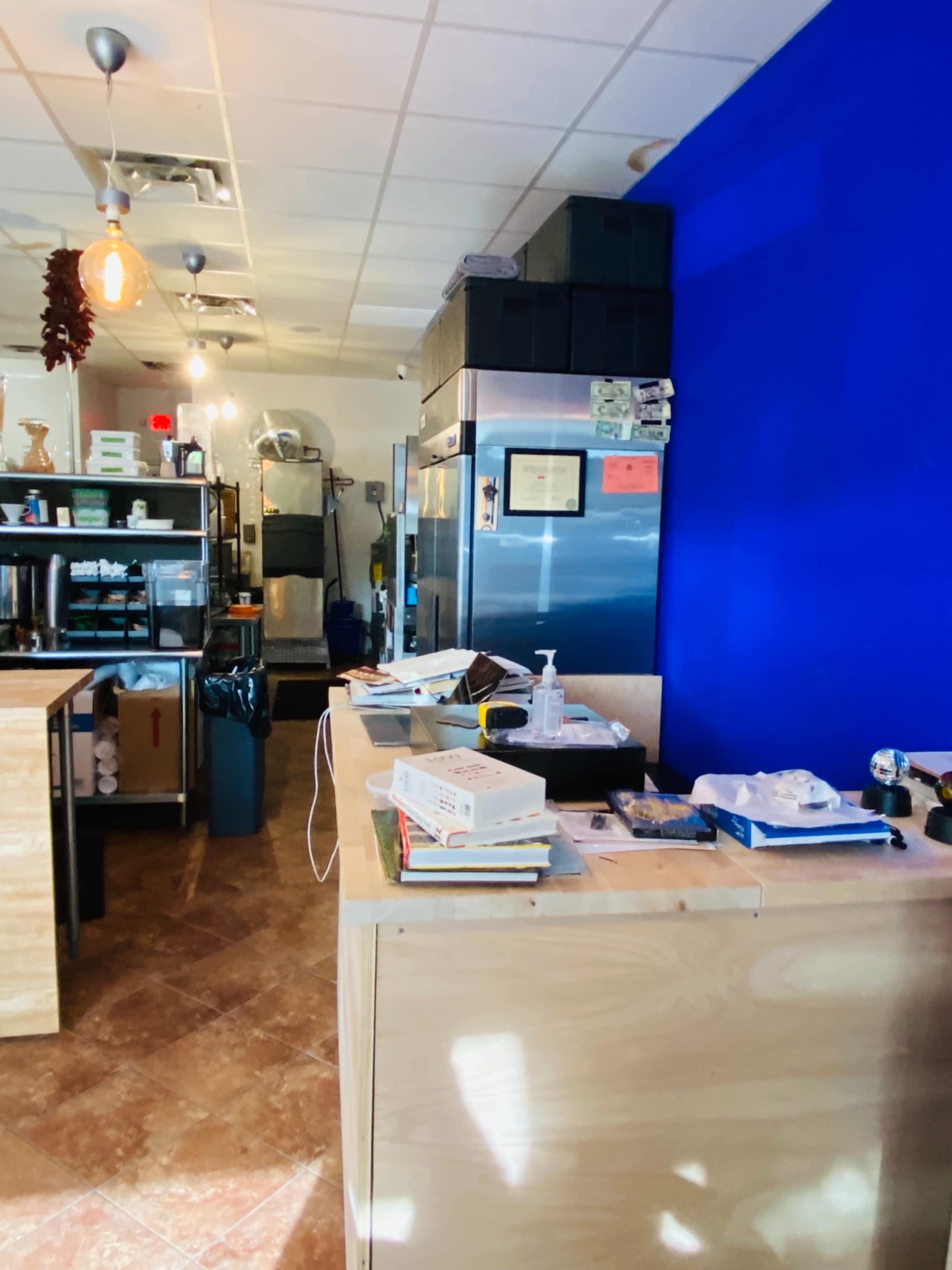 The image shows a small kitchen space with wooden counters, a blue wall, stainless steel appliances, and various items scattered across the surfaces.