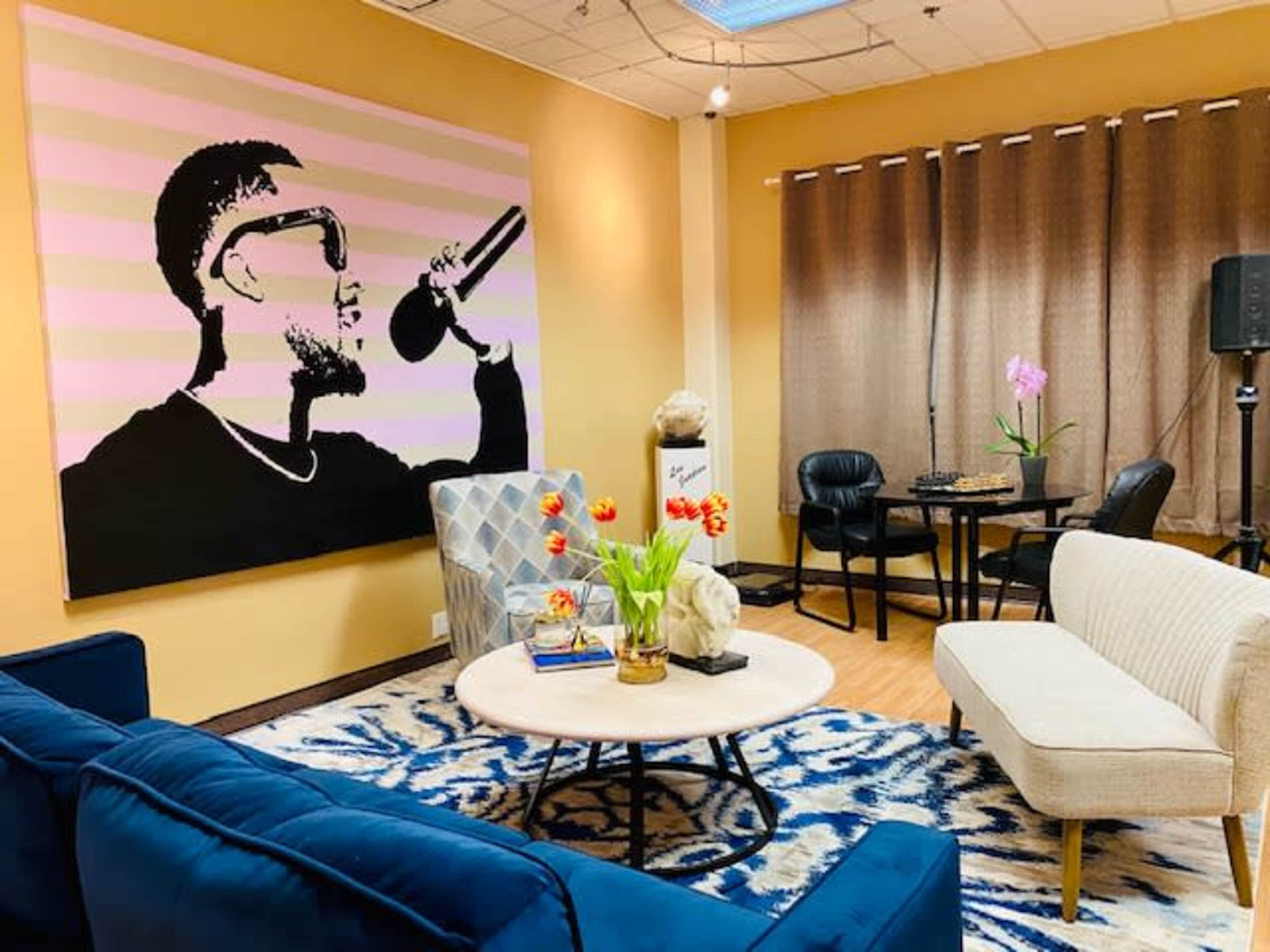 The image shows a modern lounge area featuring a large wall mural of a person with sunglasses holding a microphone, surrounded by seating and decorative elements.