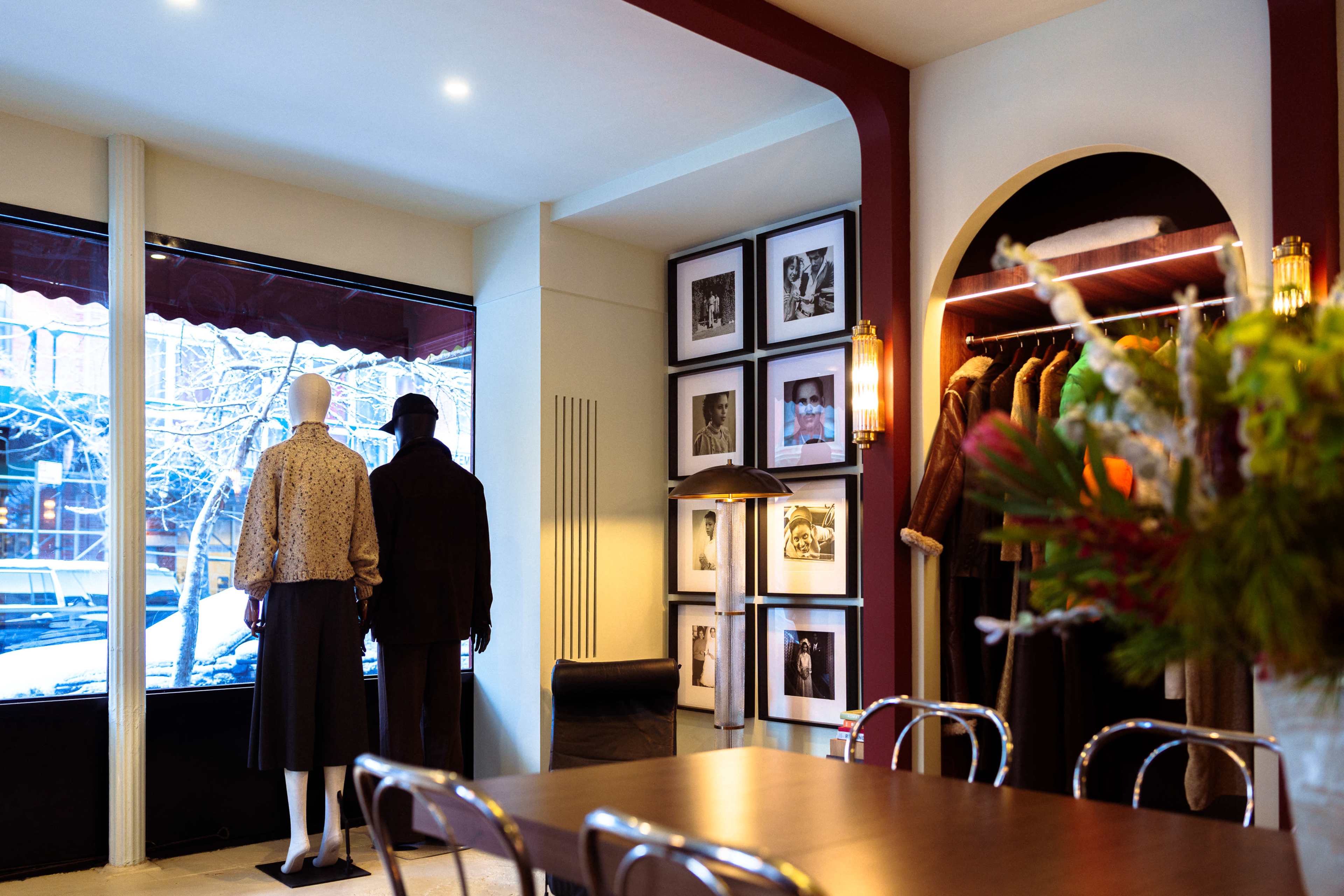 The scene shows a boutique with mannequins dressed in clothing, facing a window, and framed photographs displayed on the wall.
