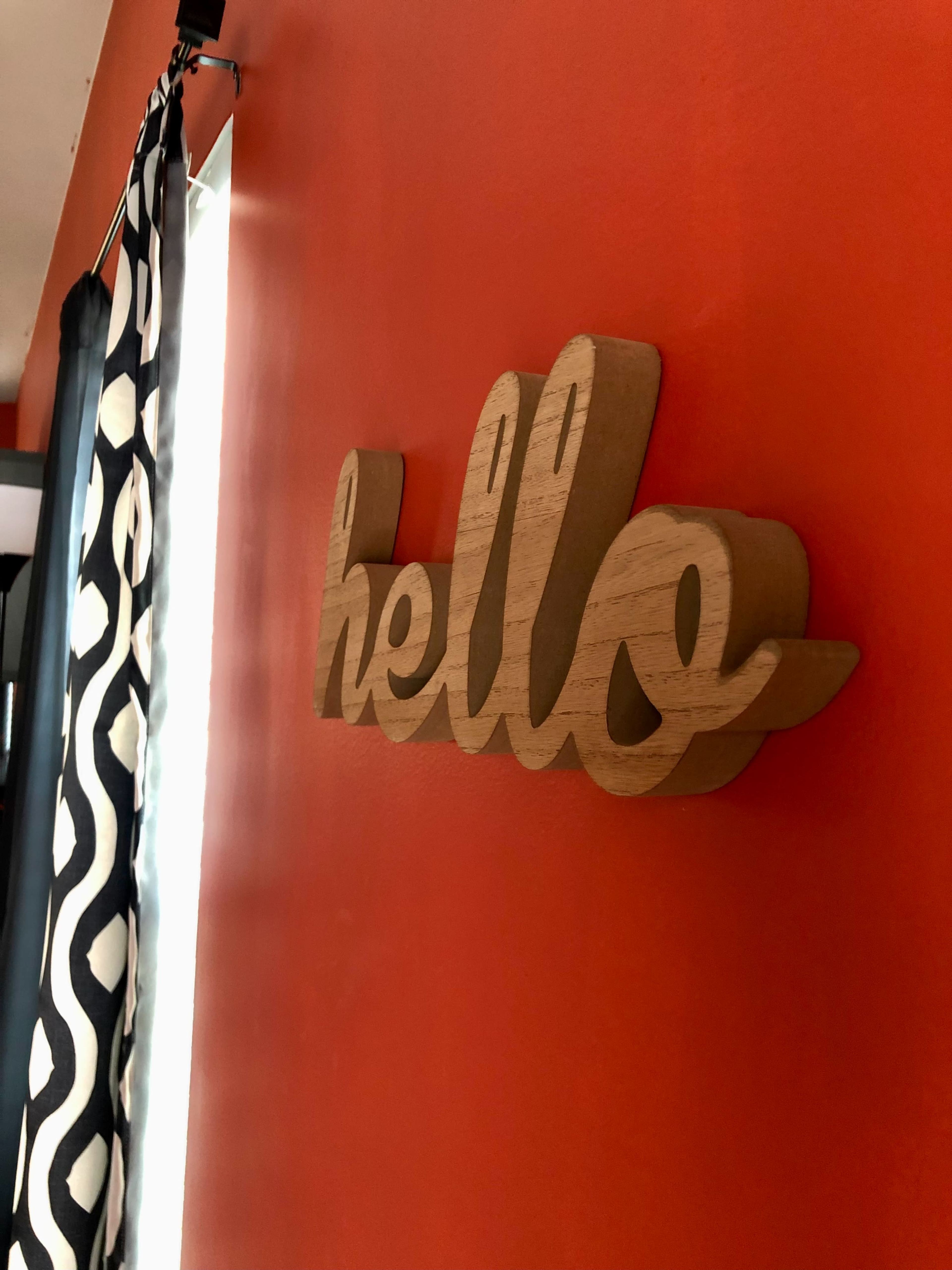 A wooden "hello" sign is mounted on a bright orange wall beside patterned curtains.
